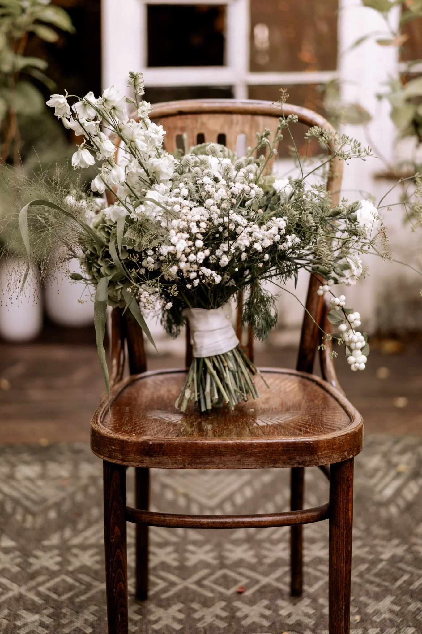 Ein Brautstrauß mit weißen und grünen Pflanzen auf einem alten Holzstuhl