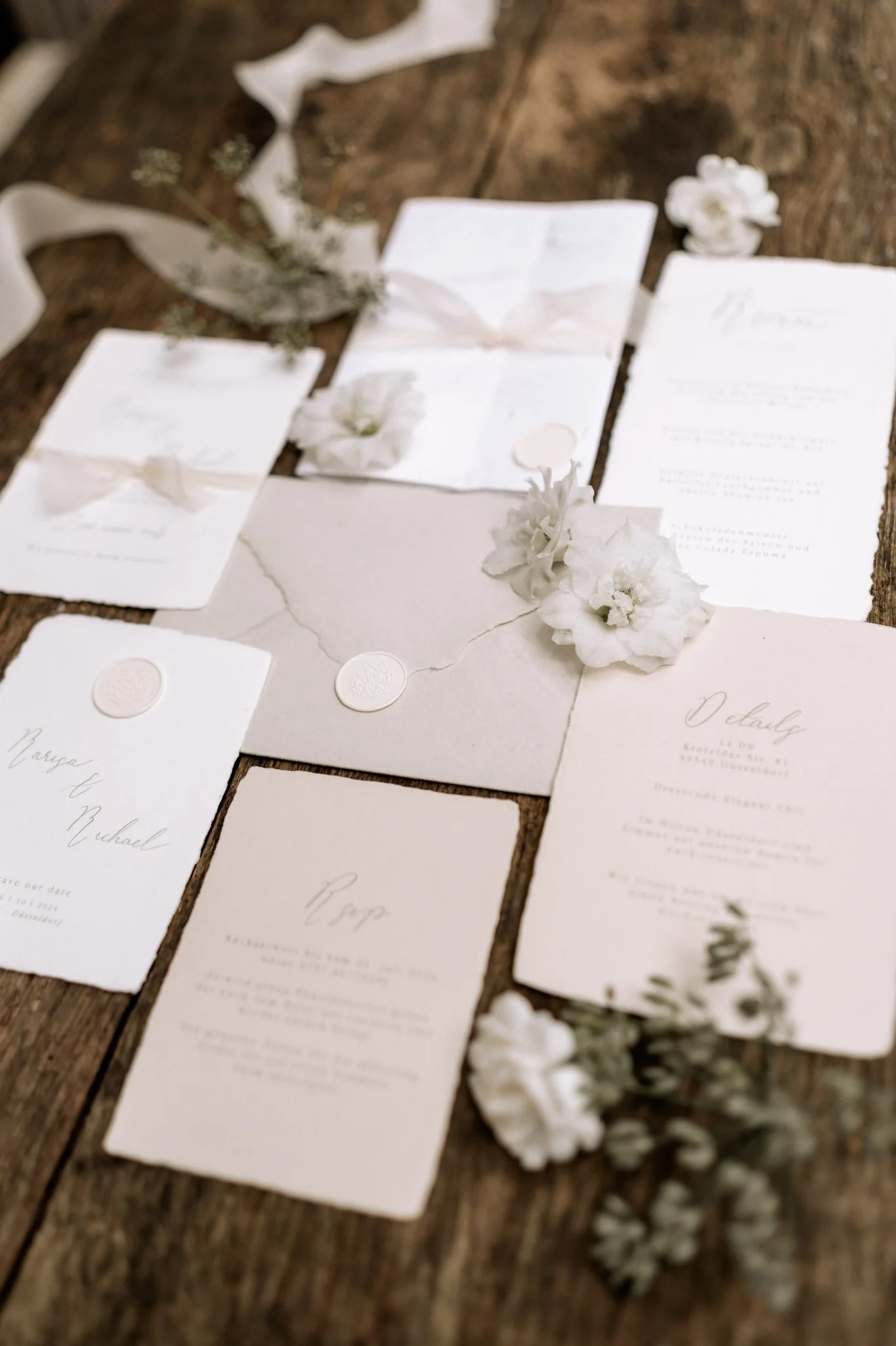 Hochzeits-Einladungen und -Karten auf einem Holz Tisch, dekoriert mit weißen Blumen und Wachssiegeln.