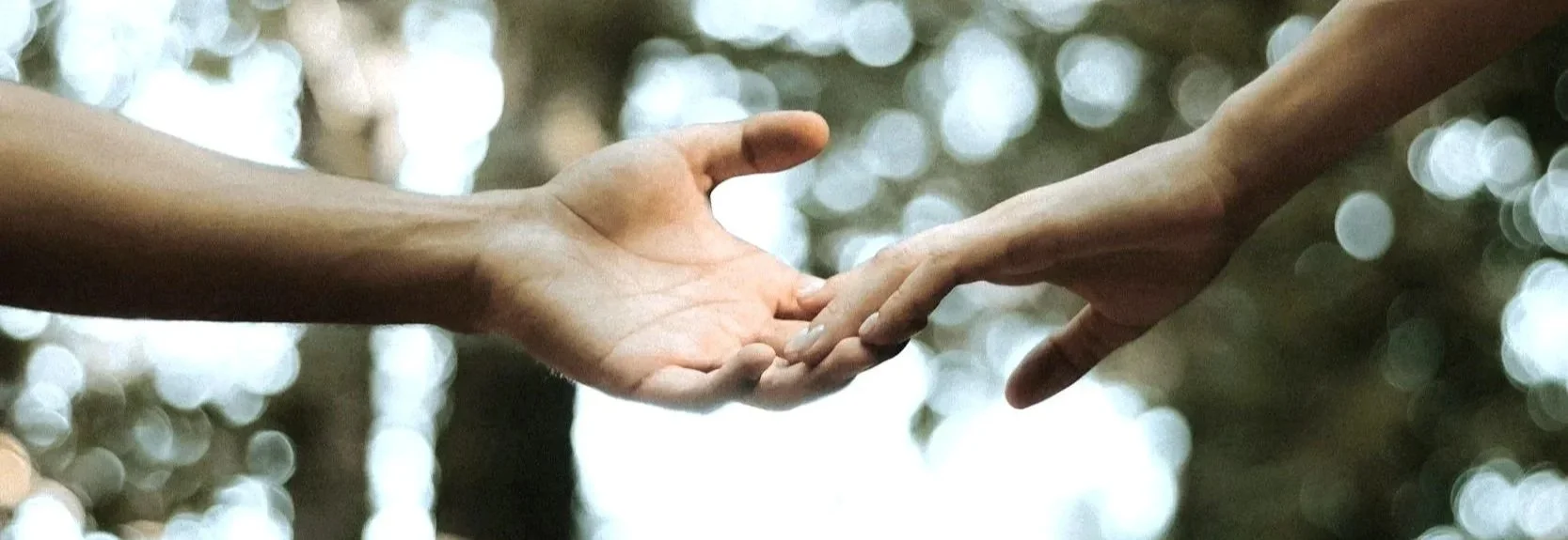Two people reaching toward each other’s hands outdoors.