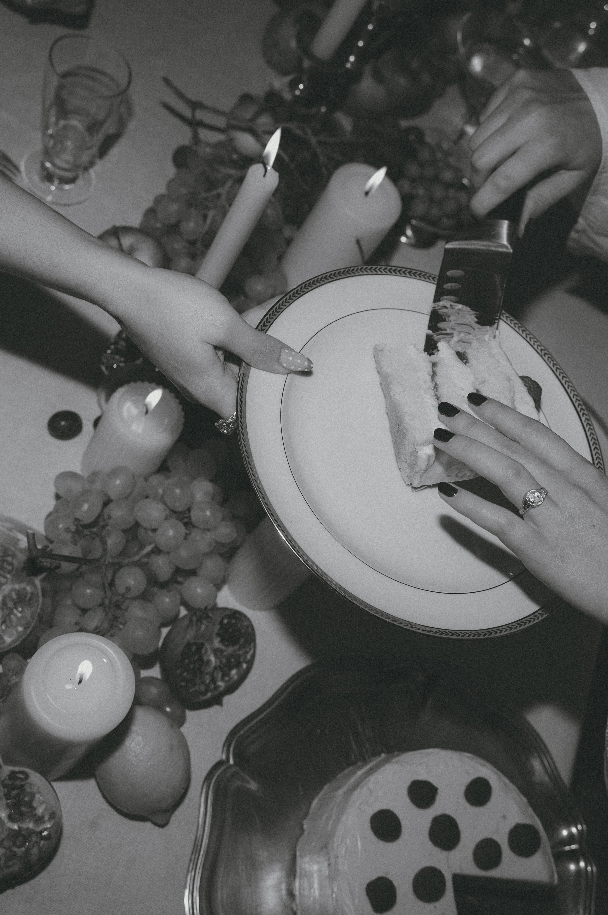 Une pause fête avec une part de gâteau sur une assiette, des mains qui la tiennent, entourée de bougies, de fruits et d'autres gâteaux.