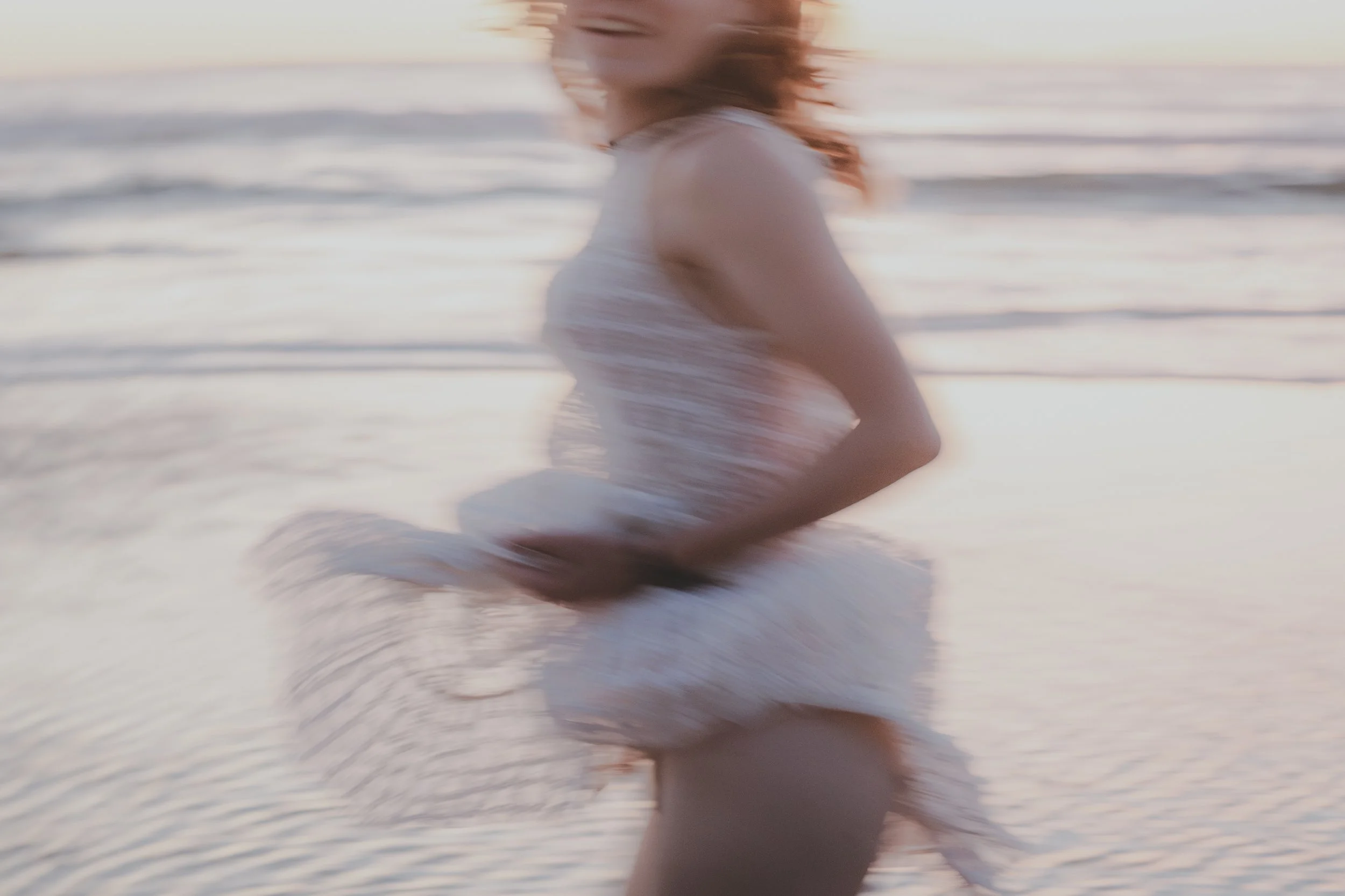 Une femme portant une robe blanche court sur la plage au coucher du soleil, avec la mer en arrière-plan.