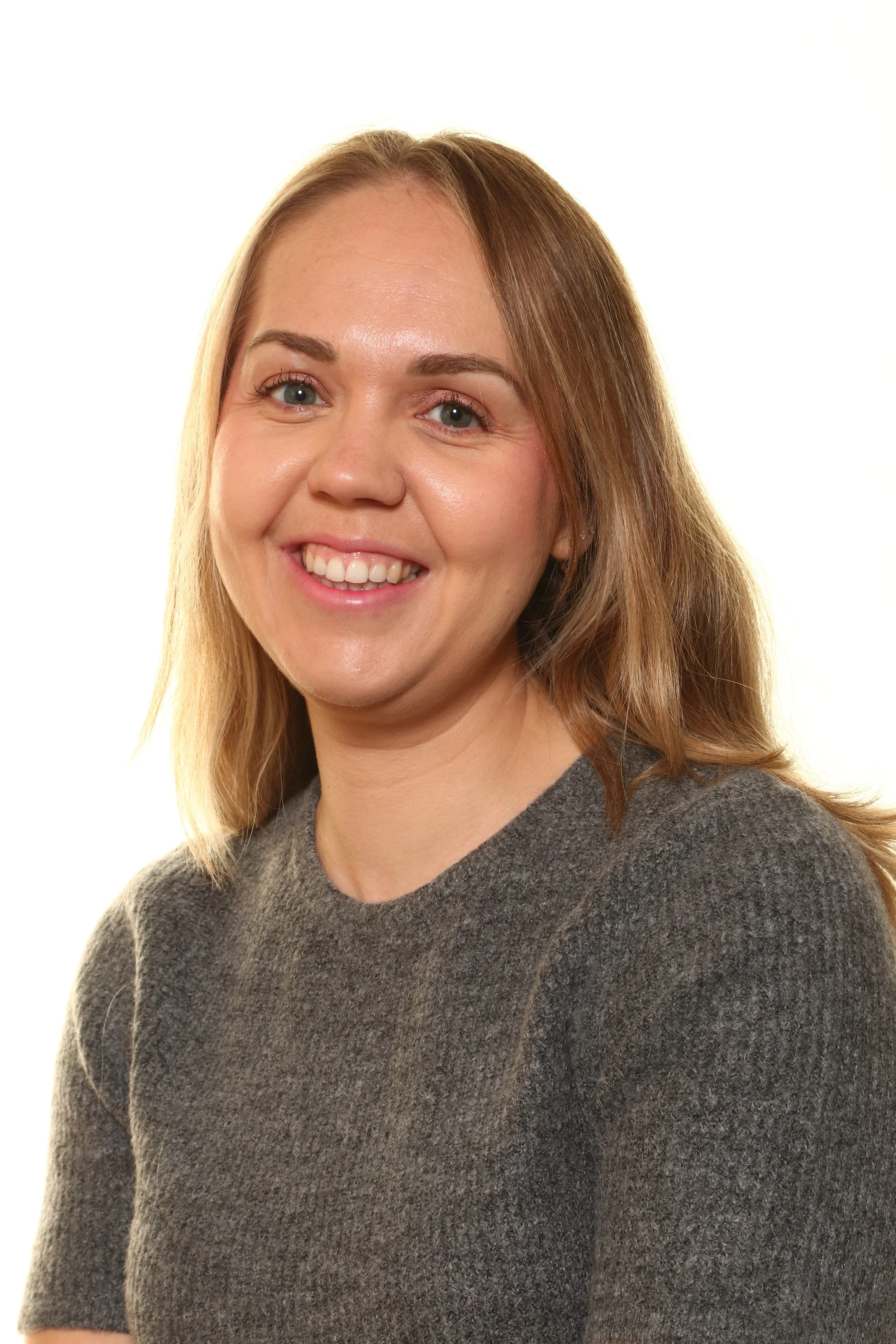 Older man with glasses smiling outdoors in front of green foliage, wearing a light blue short-sleeved shirt.