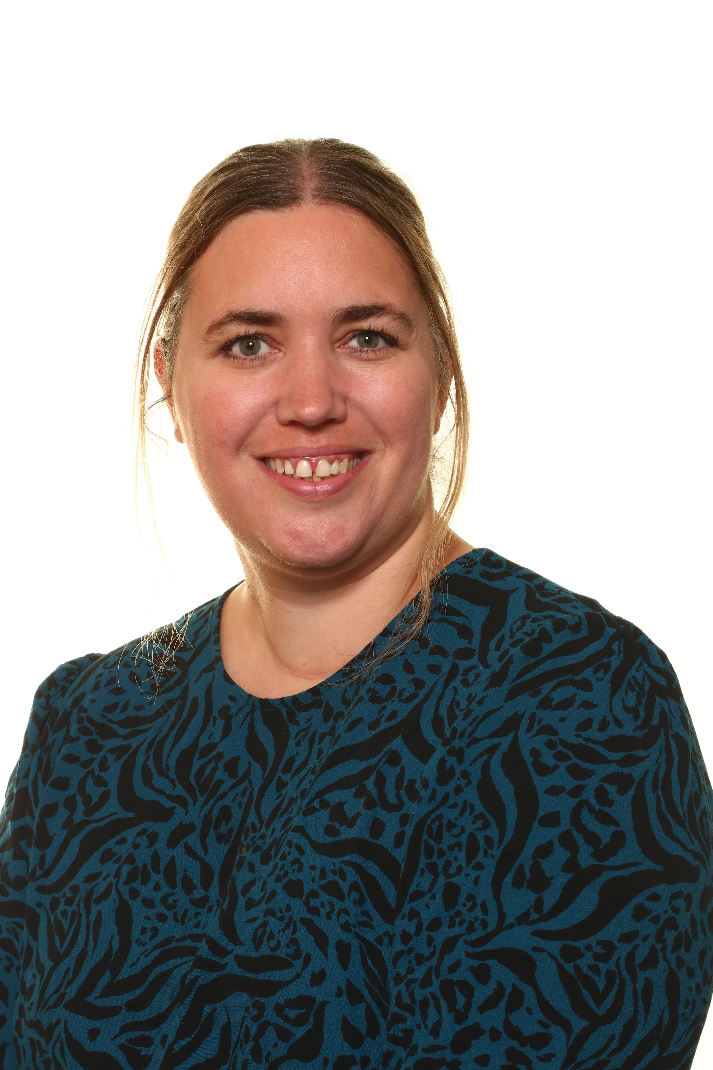 Close-up of a woman with red hair, smiling, wearing a black and green top, against a yellow background.