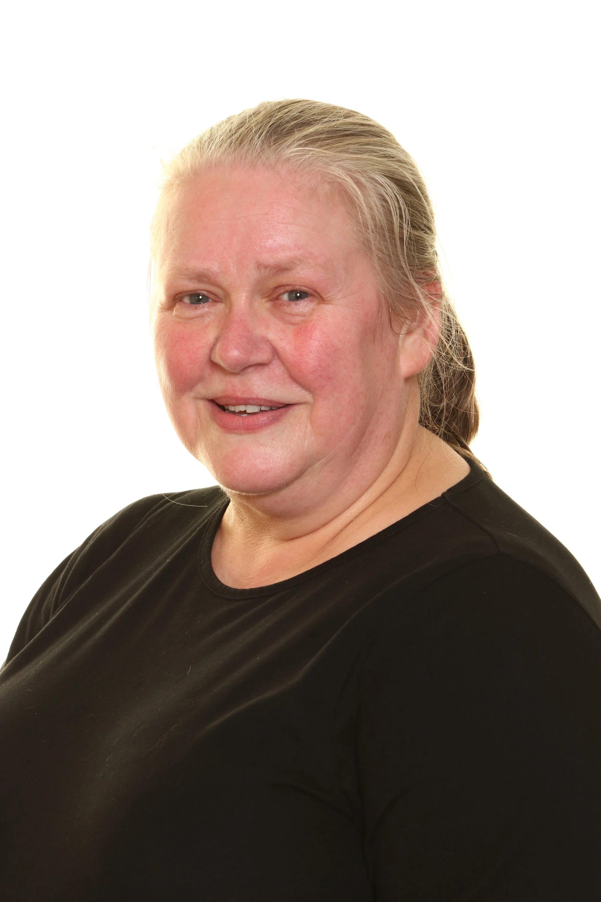 Close-up portrait of a woman with dark hair, wearing a denim shirt, smiling slightly, in front of a plain white door.