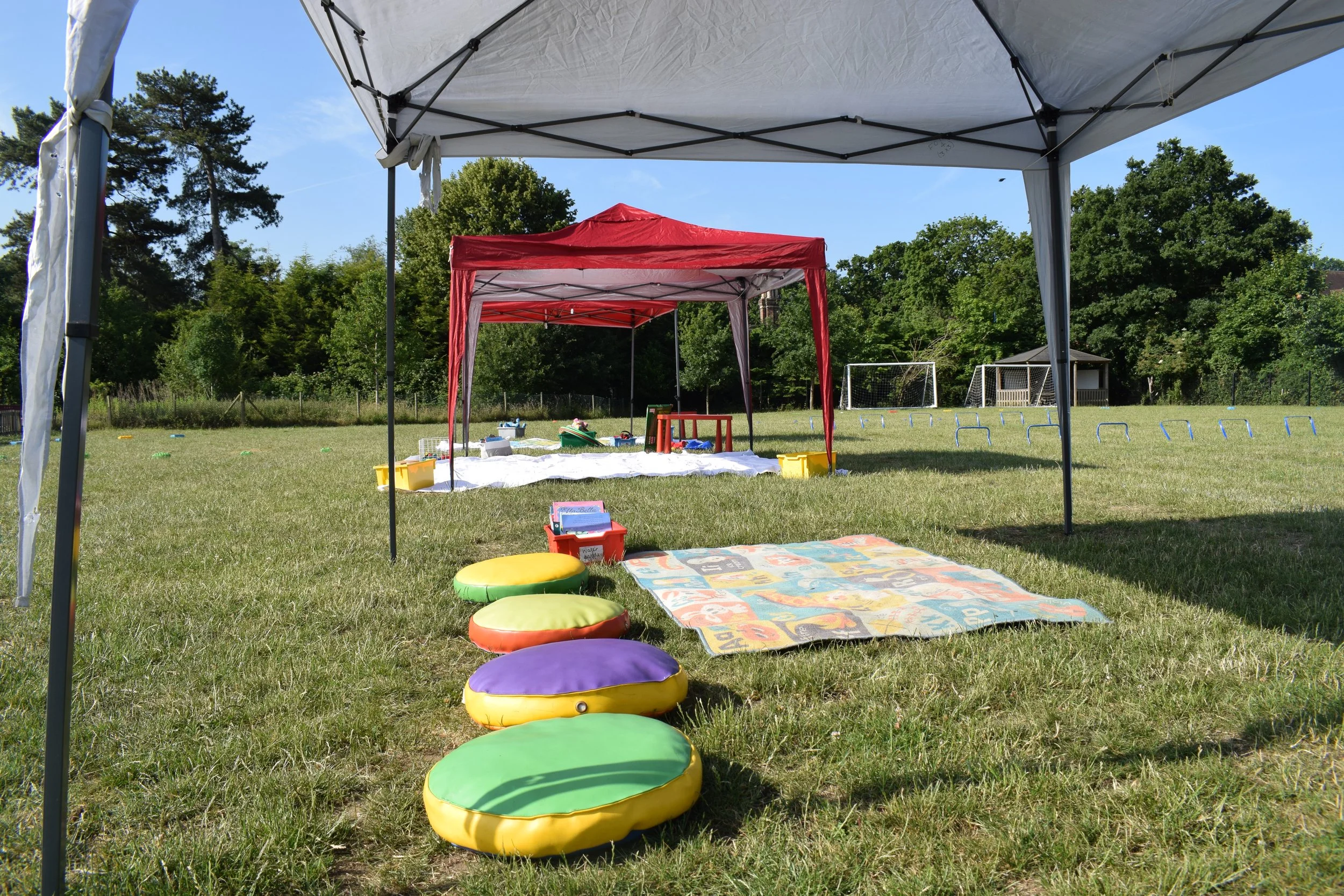 Outdoor setup with tents, colorful cushions, and toys on grass field, possibly for a children's event or activity.
