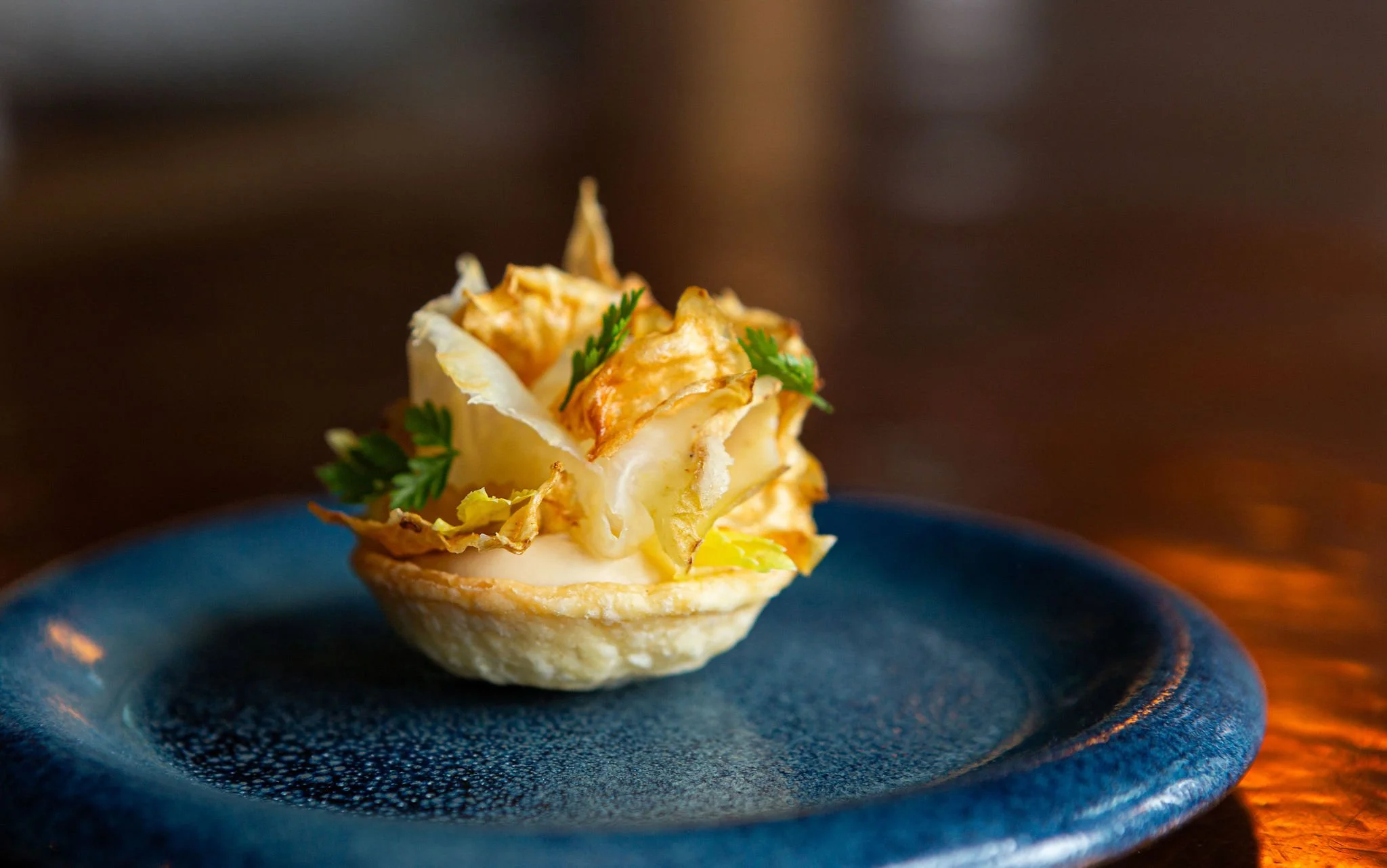 A savory tart shell filled with creamy cheese, topped with caramelized onions and garnished with fresh parsley, on a dark blue plate.