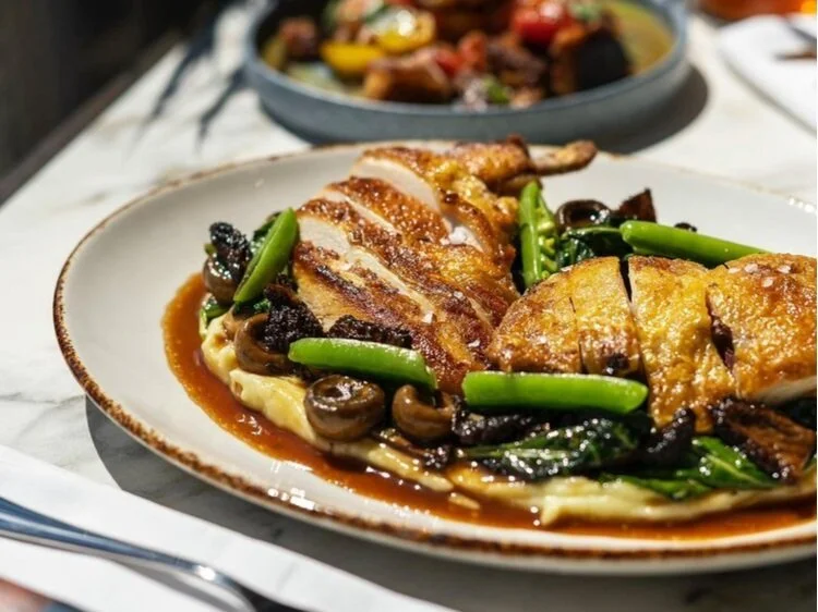 Plate of sliced grilled chicken served over mashed potatoes with sautéed mushrooms and green beans, with a dark gravy sauce.