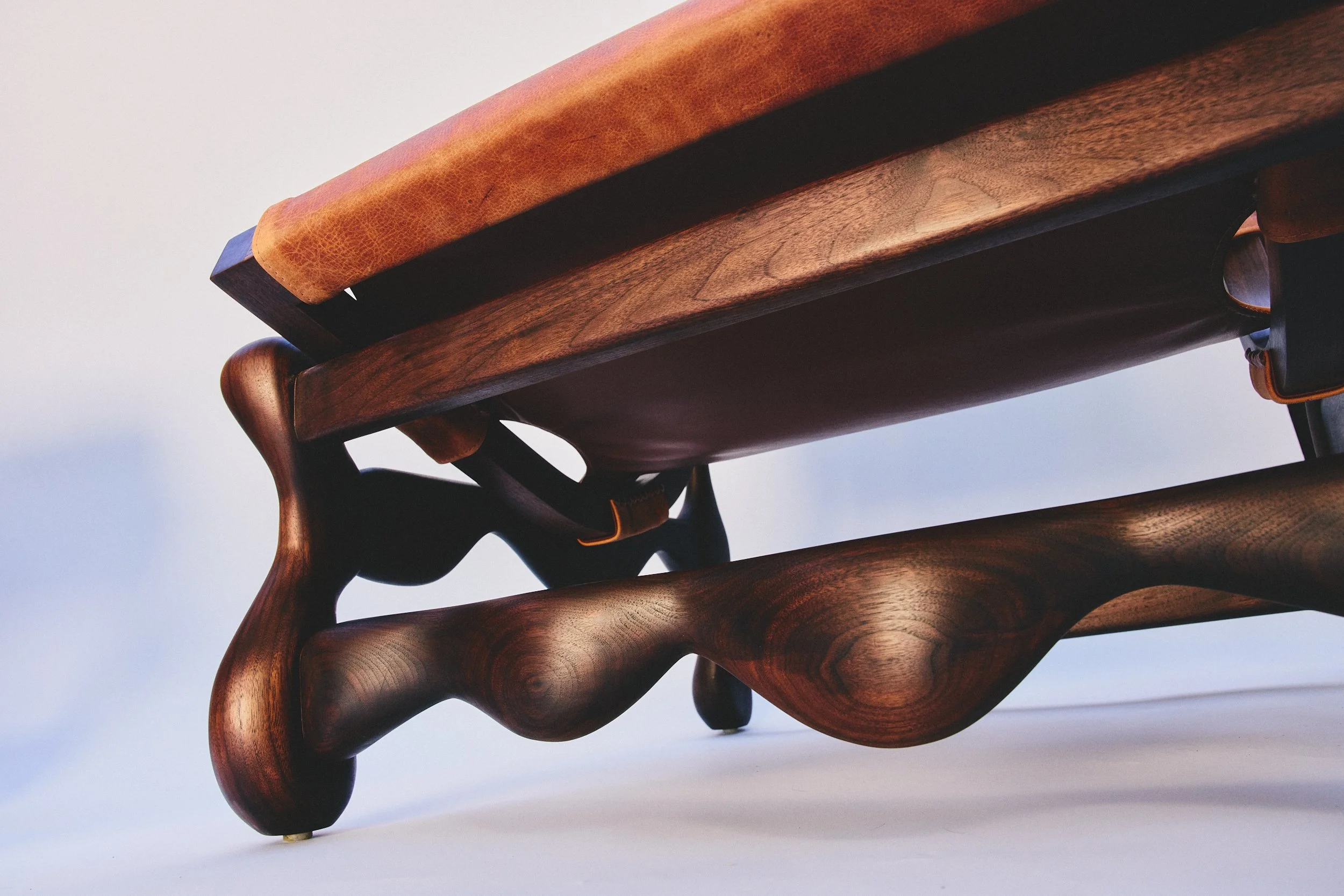 Close-up of a wooden chair with detailed craftsmanship, showing the armrest, seat, and curved legs, against a plain background.