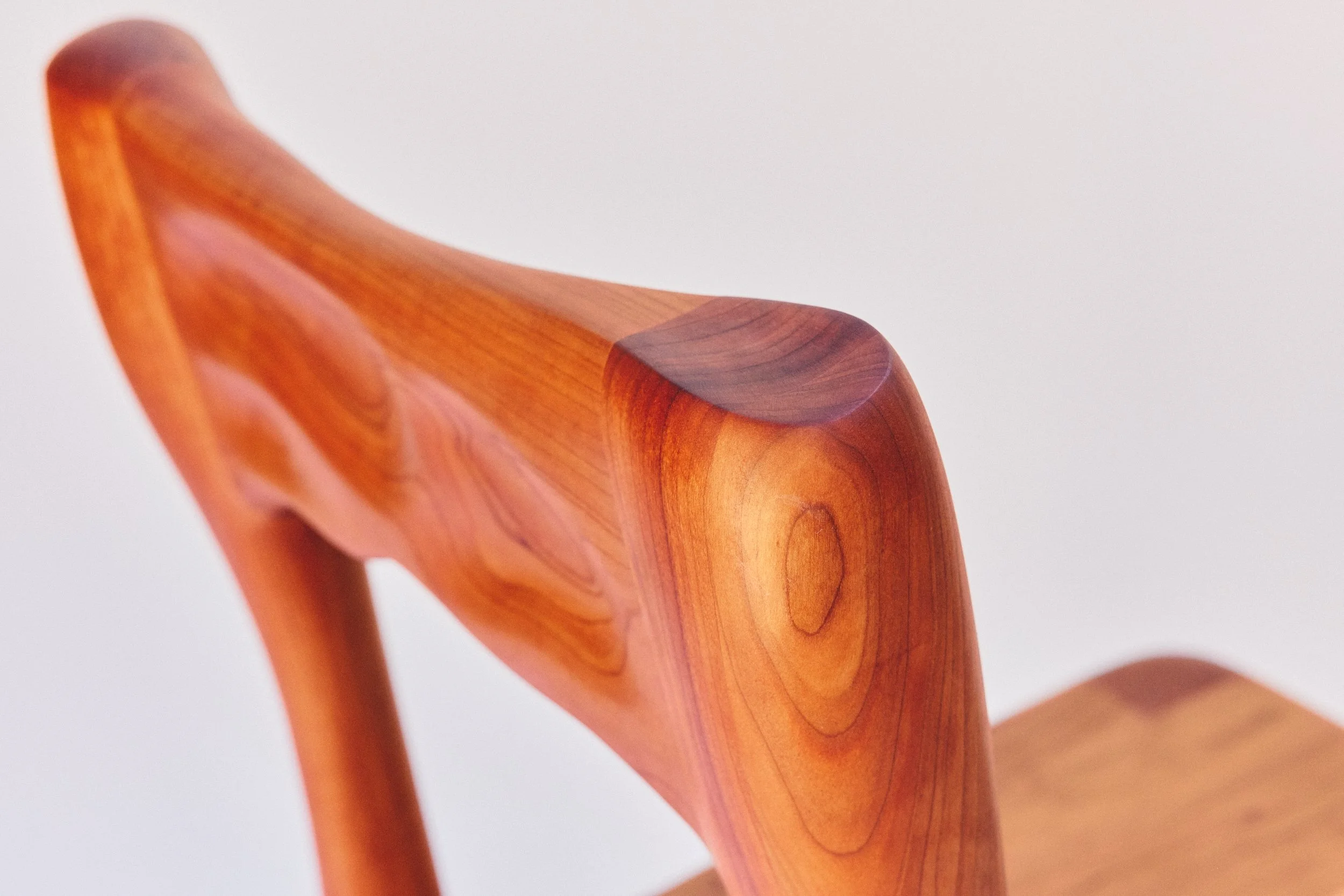 Close-up of a wooden chair with curved armrest against a plain white background.