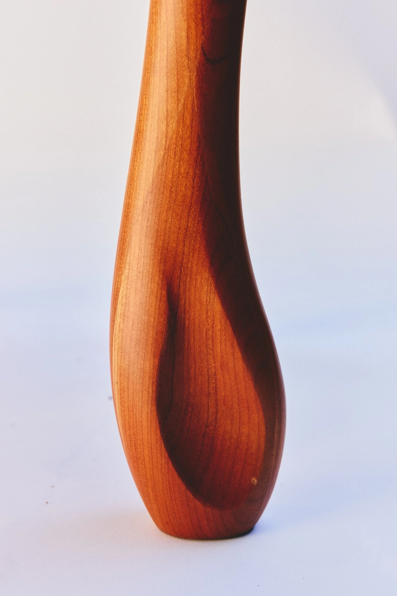 Close-up of a polished, curved wooden sculpture or piece of furniture with a smooth surface and natural wood grain, set against a plain white background.