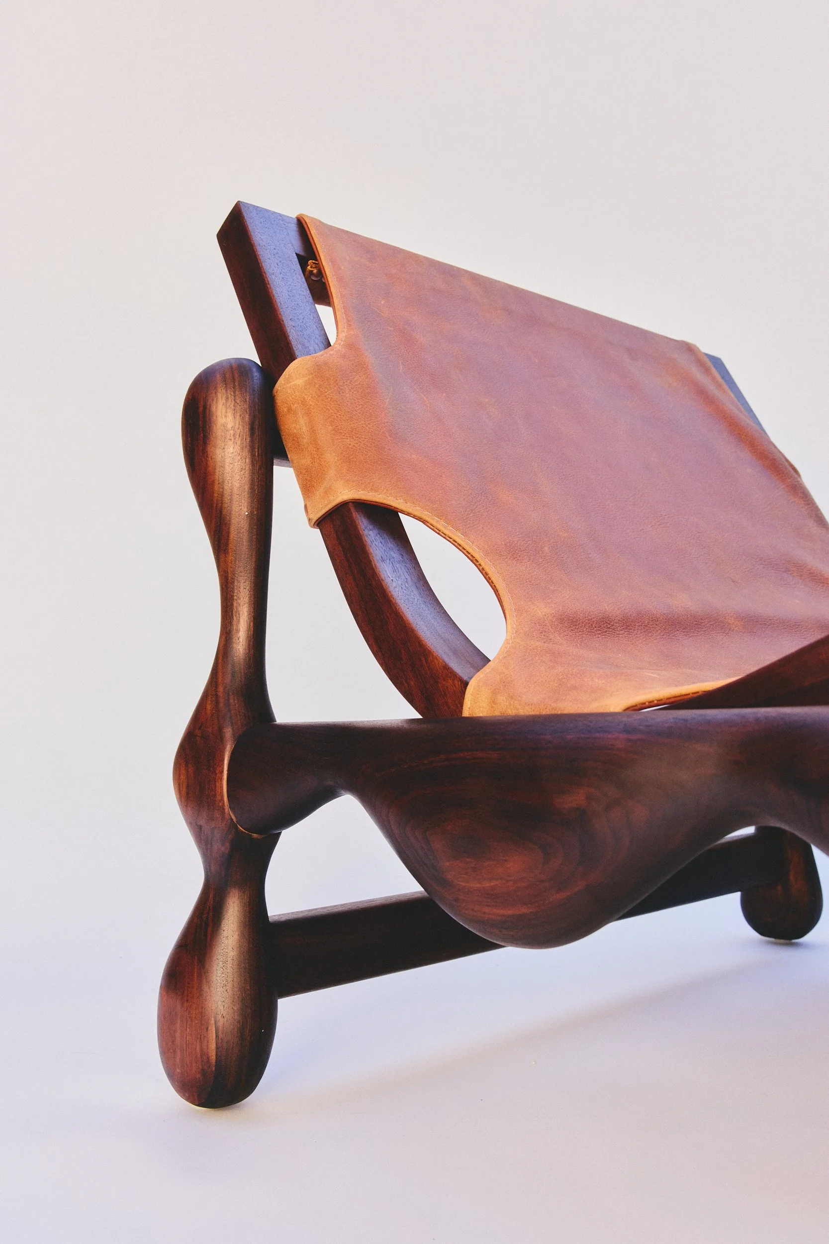 Close-up of a wooden chair with curved legs and a leather seat against a plain white background.