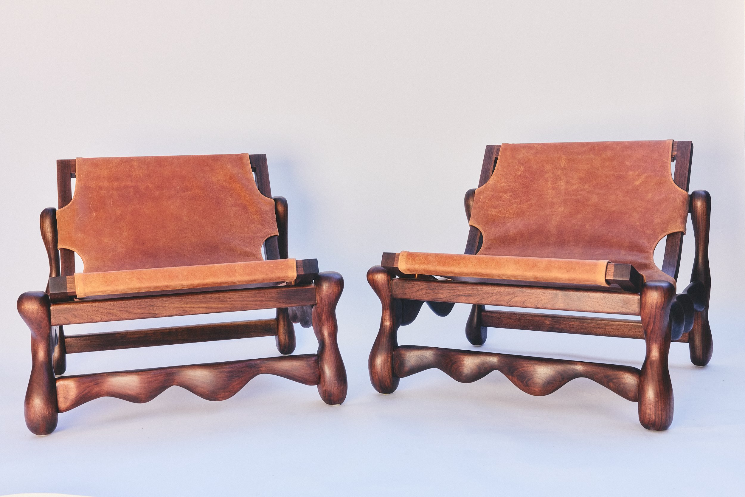 Two wooden chairs with leather seats and backs against a plain white background.