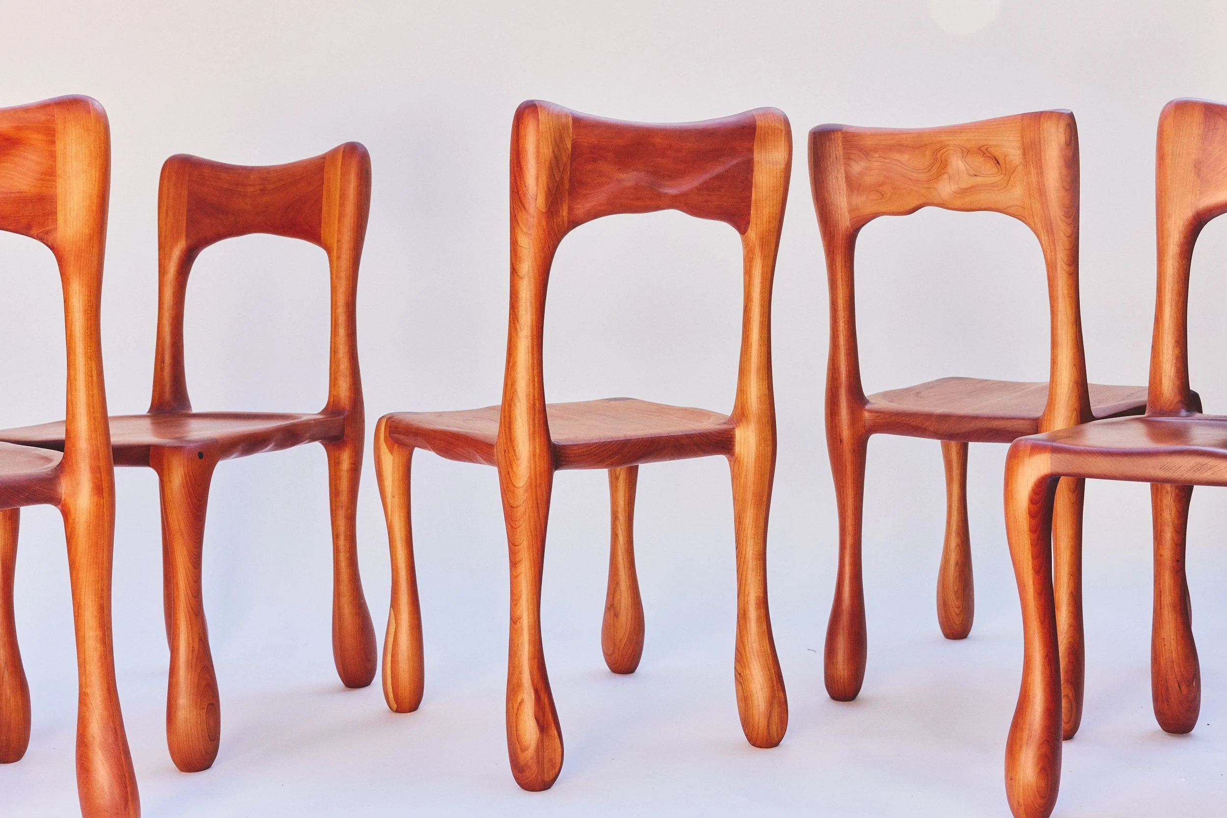 A row of five wooden chairs with curved backs and legs, set against a plain light background.