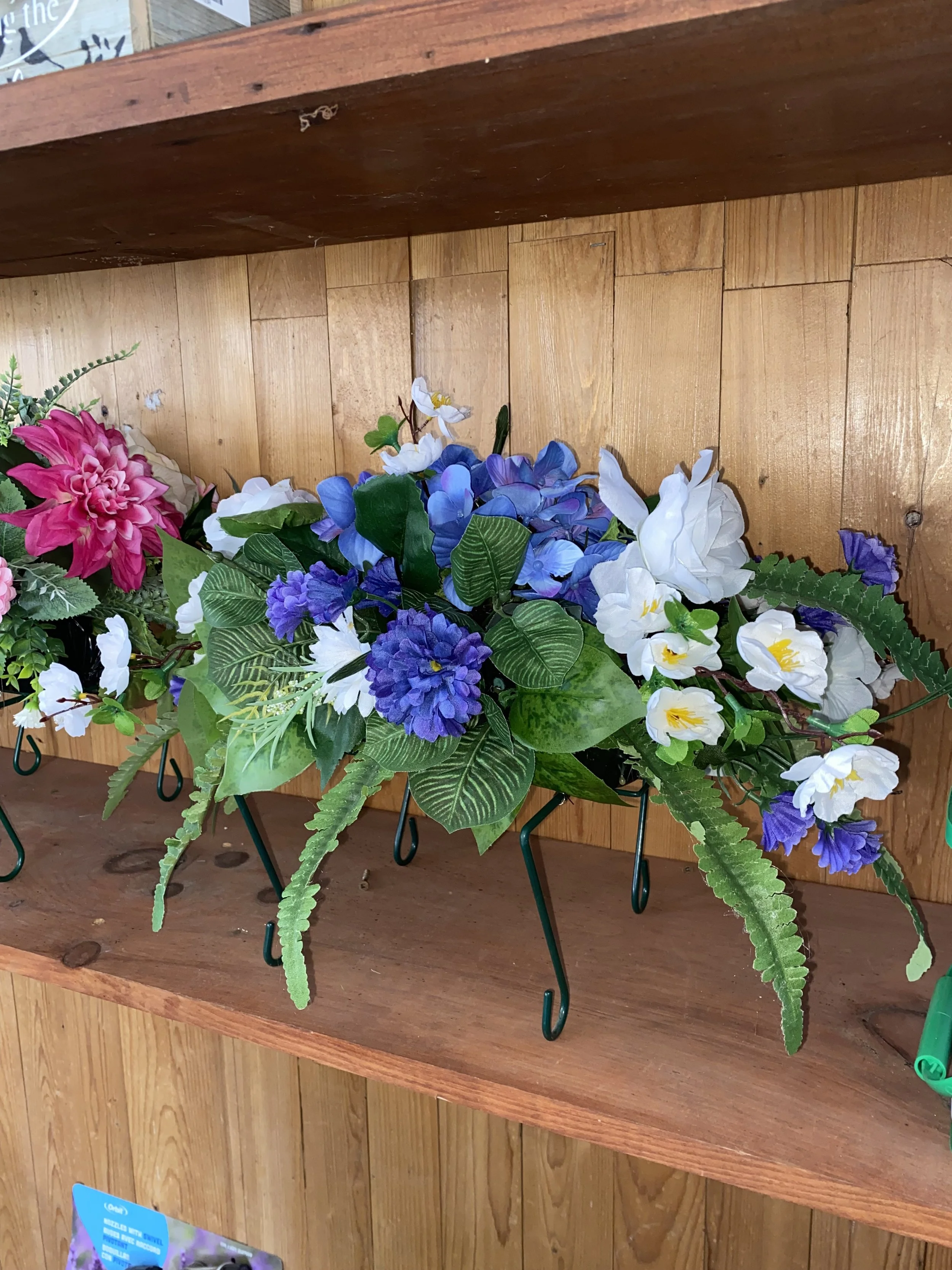 Artificial flower arrangement with white, purple, and pink flowers on a wooden shelf.