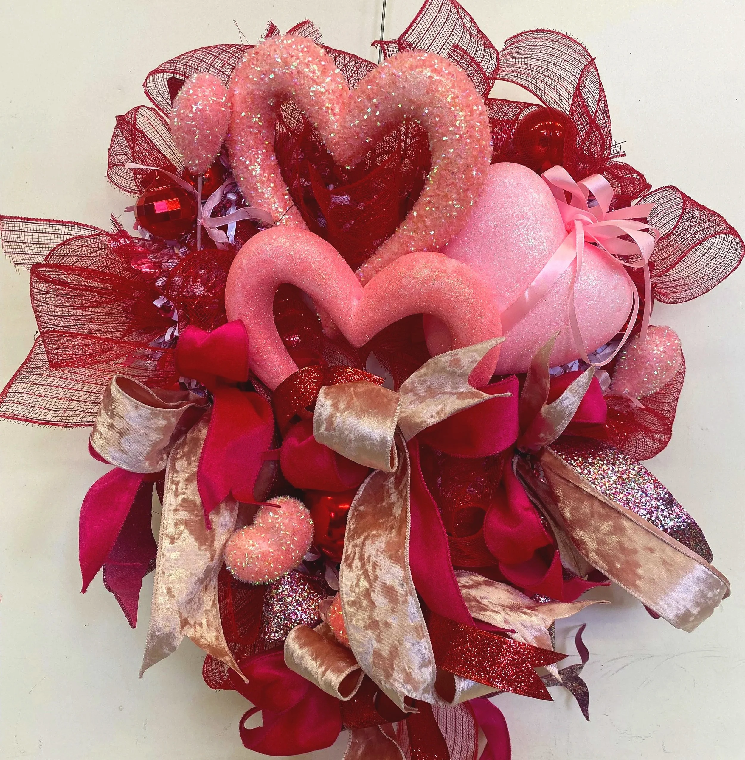 Valentine's Day themed decorative arrangement with pink and red hearts, ribbon bows, glitter, and mesh embellishments.