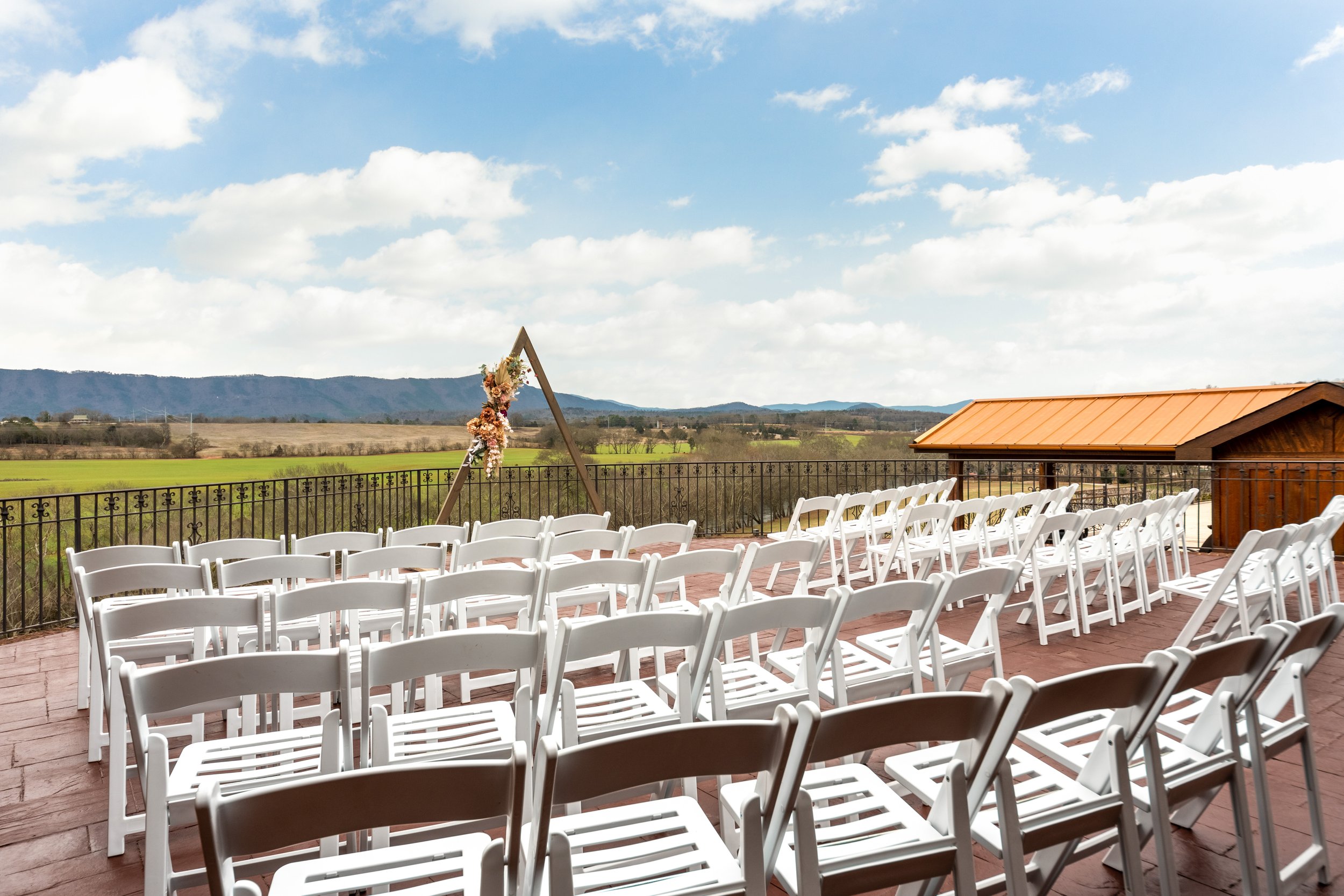 Intimate outdoor wedding venue in Tennessee. White resin chairs, simple wooden arbor with floral arrangement, overlooking mountains.