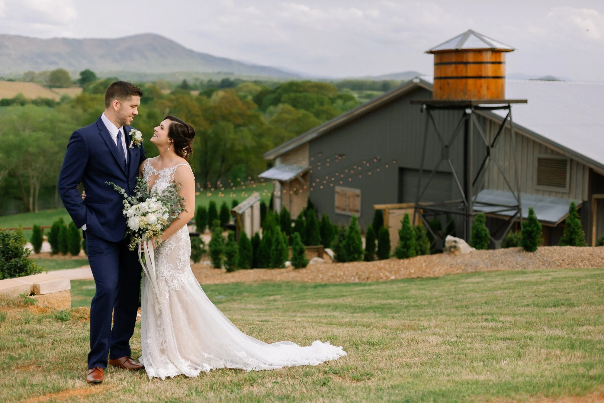 Bride and groom posing outside brown wooden wedding venue in front of East Tennessee mountains