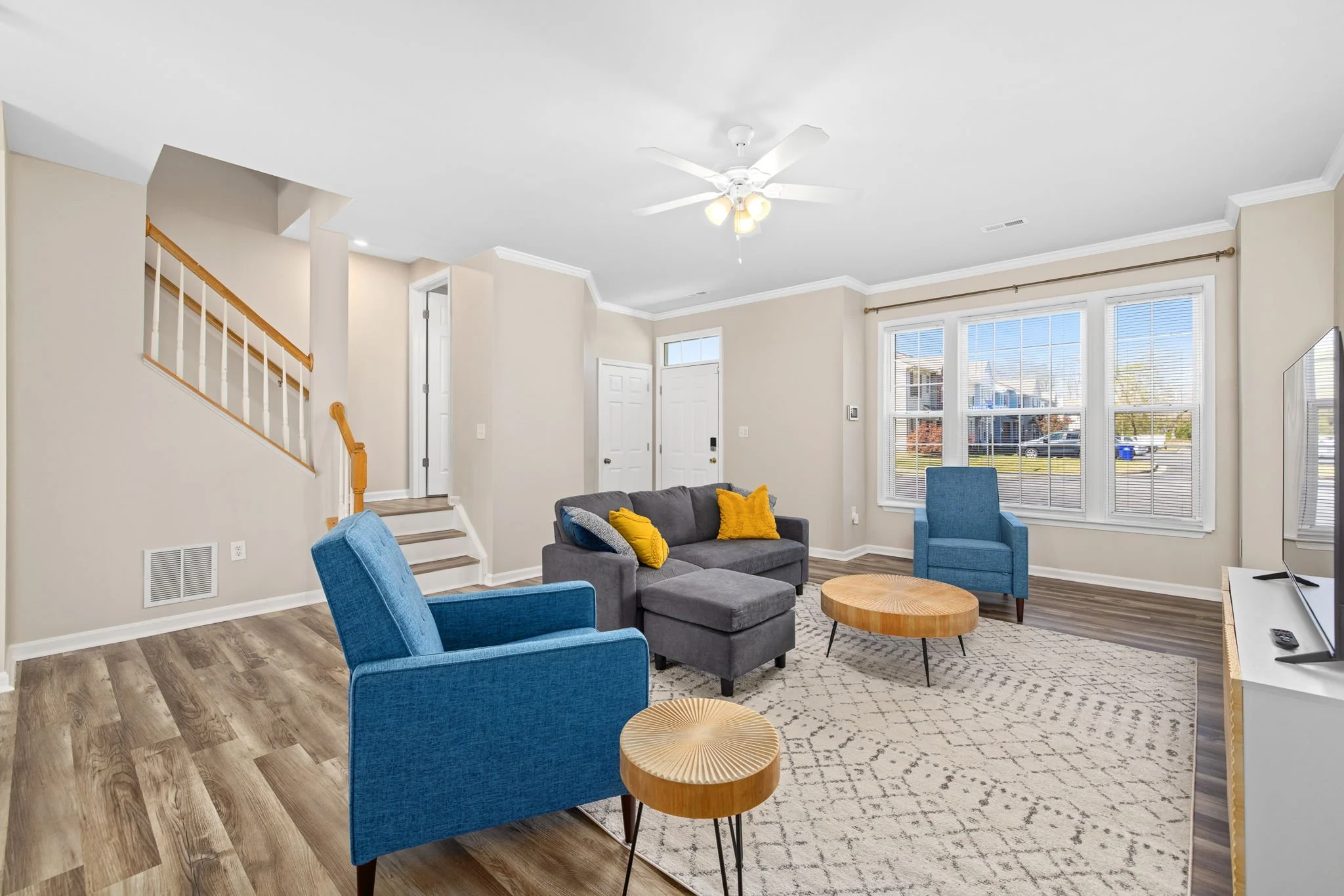 Warm inviting living room with large windows, grey sectional, blue recliner chairs and wooden coffee table. Smart tv.