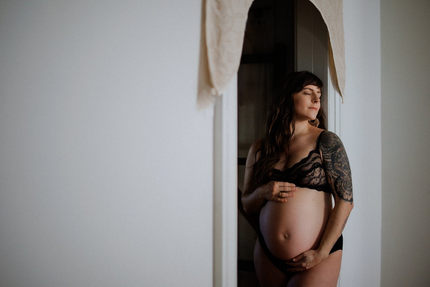 Pregnant woman in a black lace bra standing near a white archway