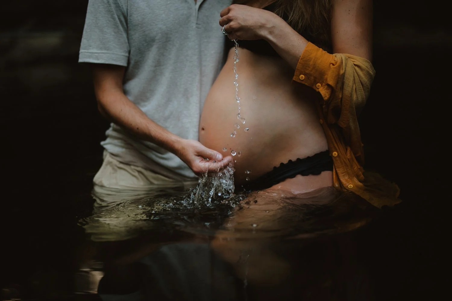 Close-up of a partner pouring water over a pregnant belly