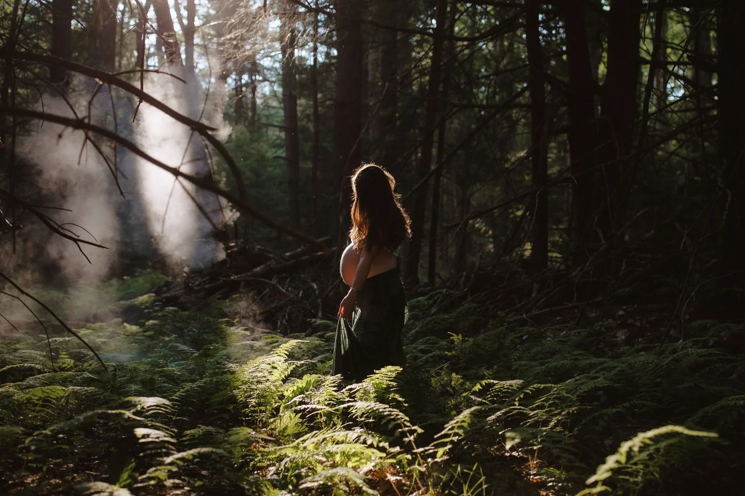 Ethereal portrait of a pregnant woman standing in a misty forest surrounded by ferns