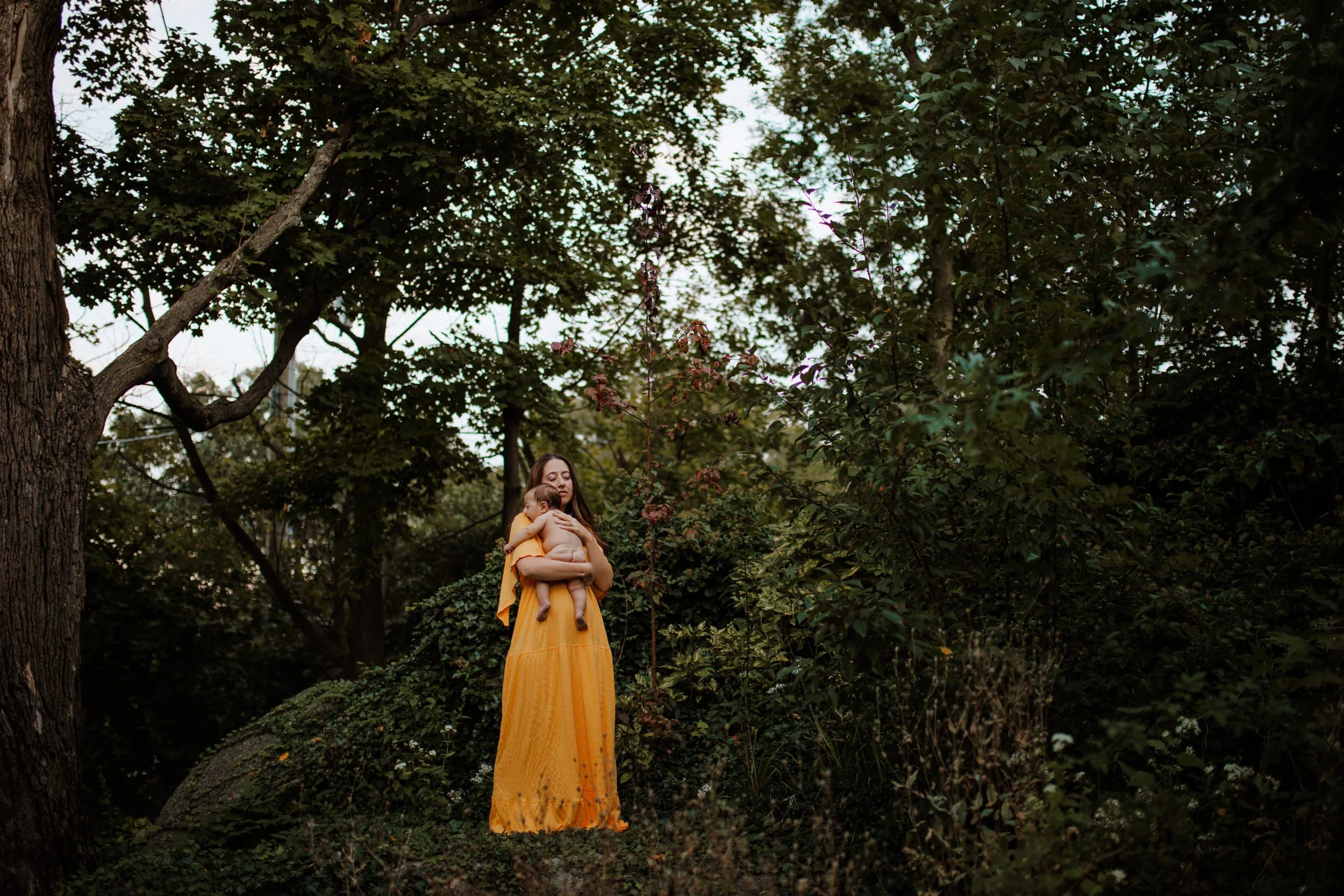 Mother in a yellow dress holding her baby in a wooded clearing, baby photographer portrait session