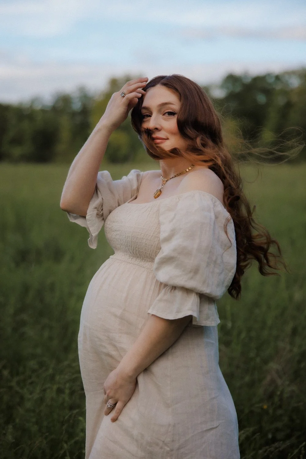 Romantic portrait of a pregnant woman in a flowing linen dress with windswept hair in an open field