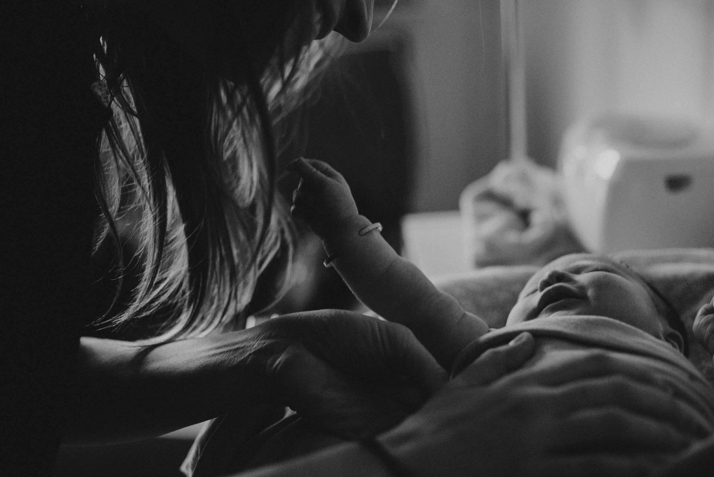 Black and white close-up of hands gently holding a newborn's feathery details, evoking a tender first moments feel.