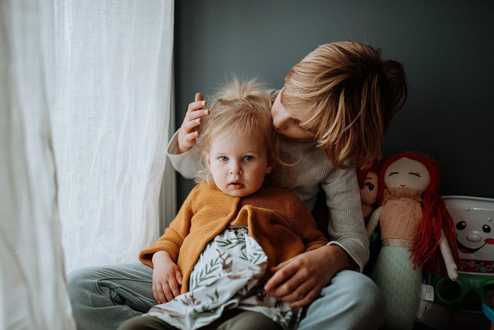 Older brother kissing his little sister's head in a cozy bedroom setting, family portrait session in New York