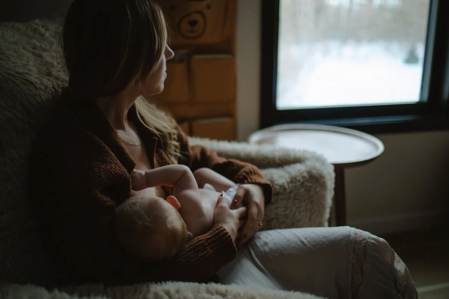 Mother nursing her newborn by a window overlooking snow, New York newborn photographer