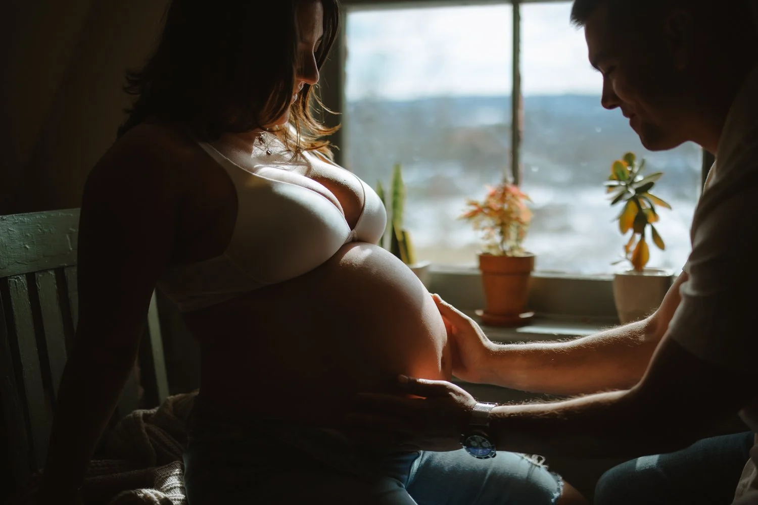 Pregnant woman and her partner sharing a quiet moment by a window with potted plants