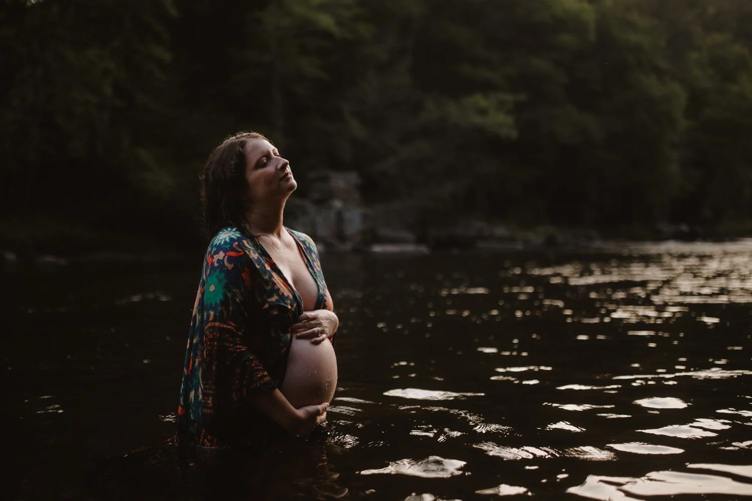 Bohemian-style portrait of a pregnant woman in a colorful kimono standing in a river