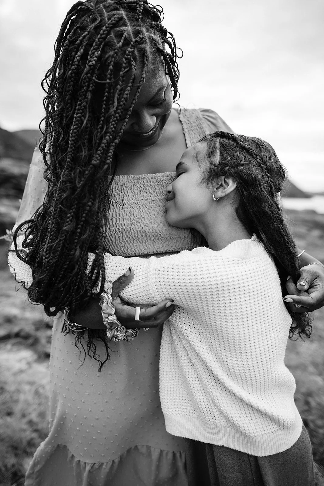 Black and white portrait of a mother and daughter embracing on a coastal bluff