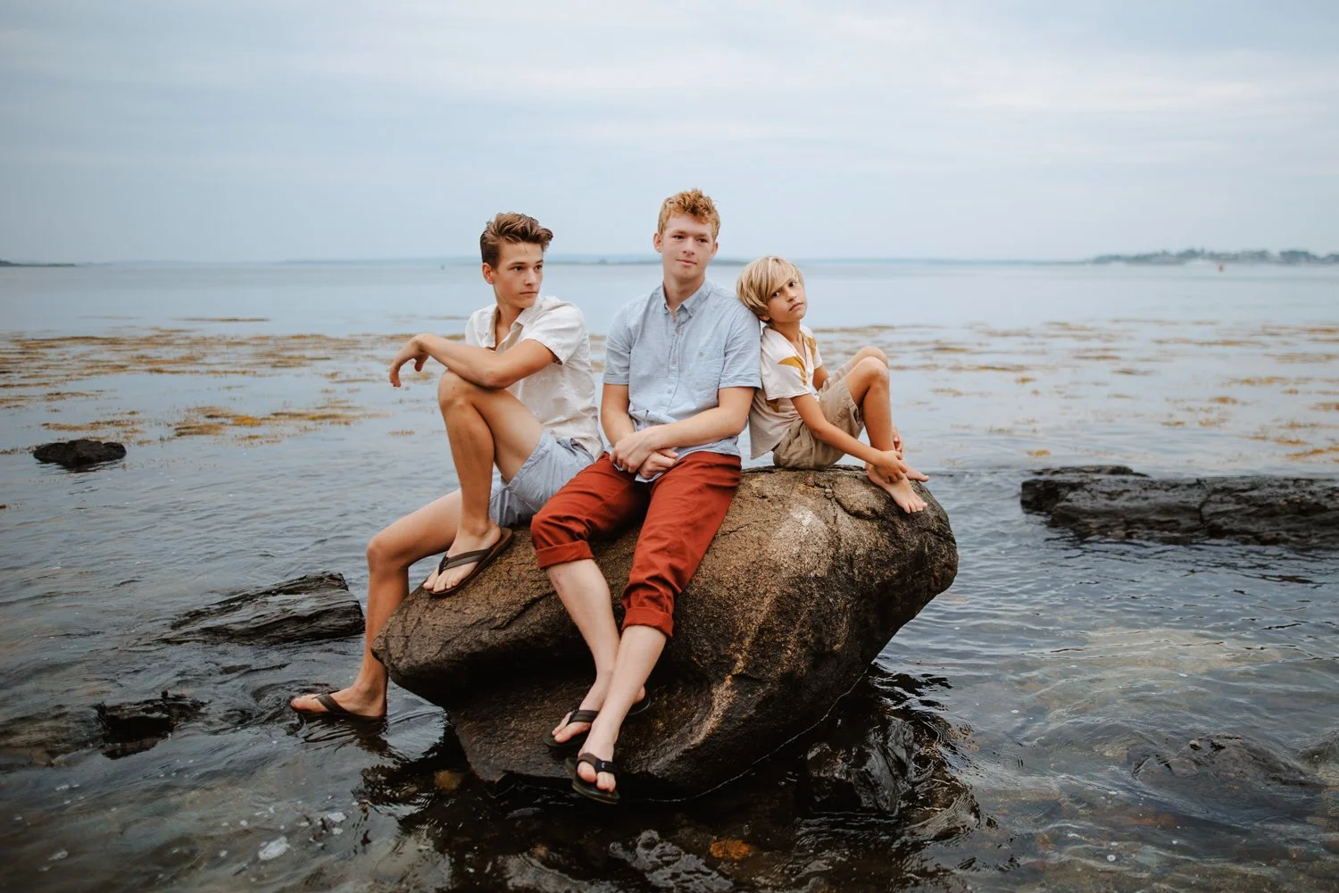 Three brothers sitting together on a large rock along the shoreline