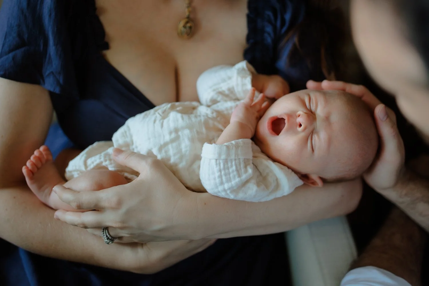 Close-up of a yawning newborn cradled in swaddled arms by both parents