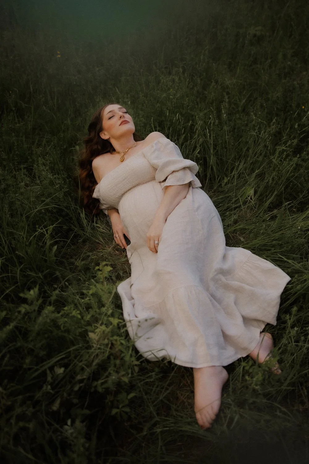 Pregnant woman leaning back with eyes closed in a dark grassy field