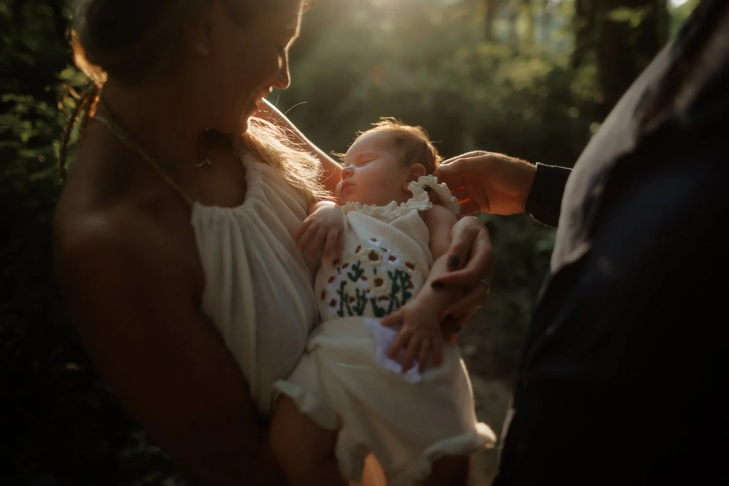 Sleeping newborn in an embroidered gown during a sunlit forest session with a New York newborn photographer