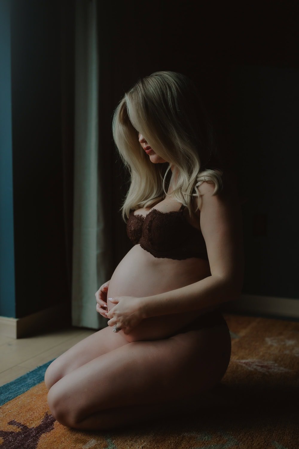 Pregnant woman in a brown lace bra sitting on the floor in soft light