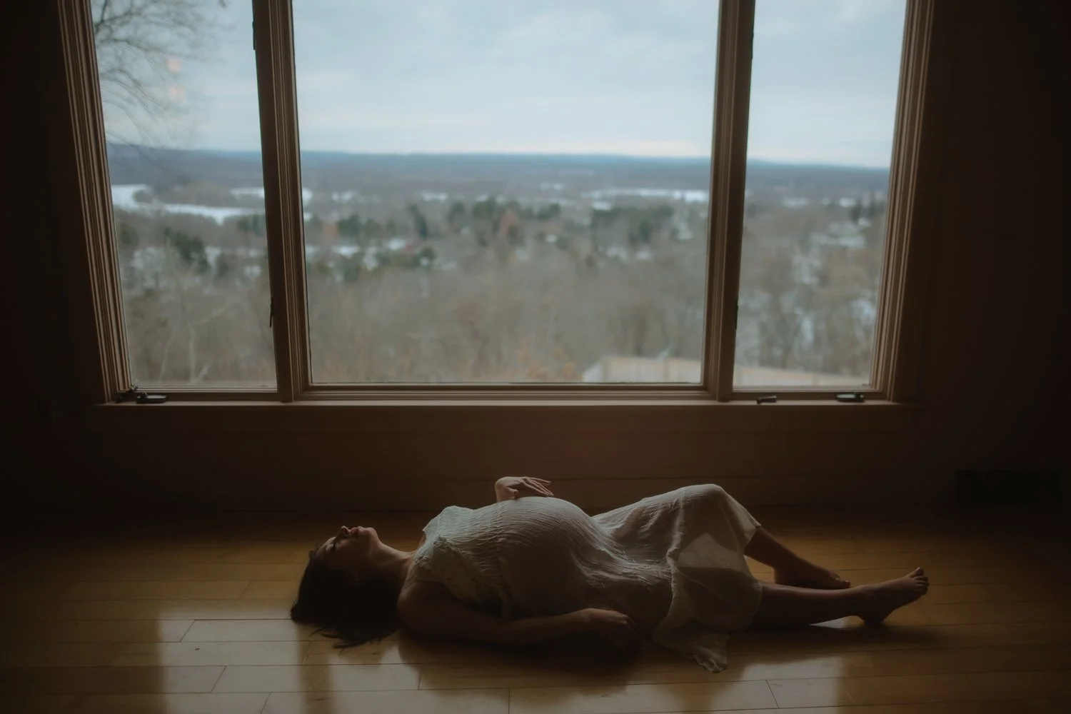 Moody portrait of a pregnant woman reclining in a dimly lit hallway