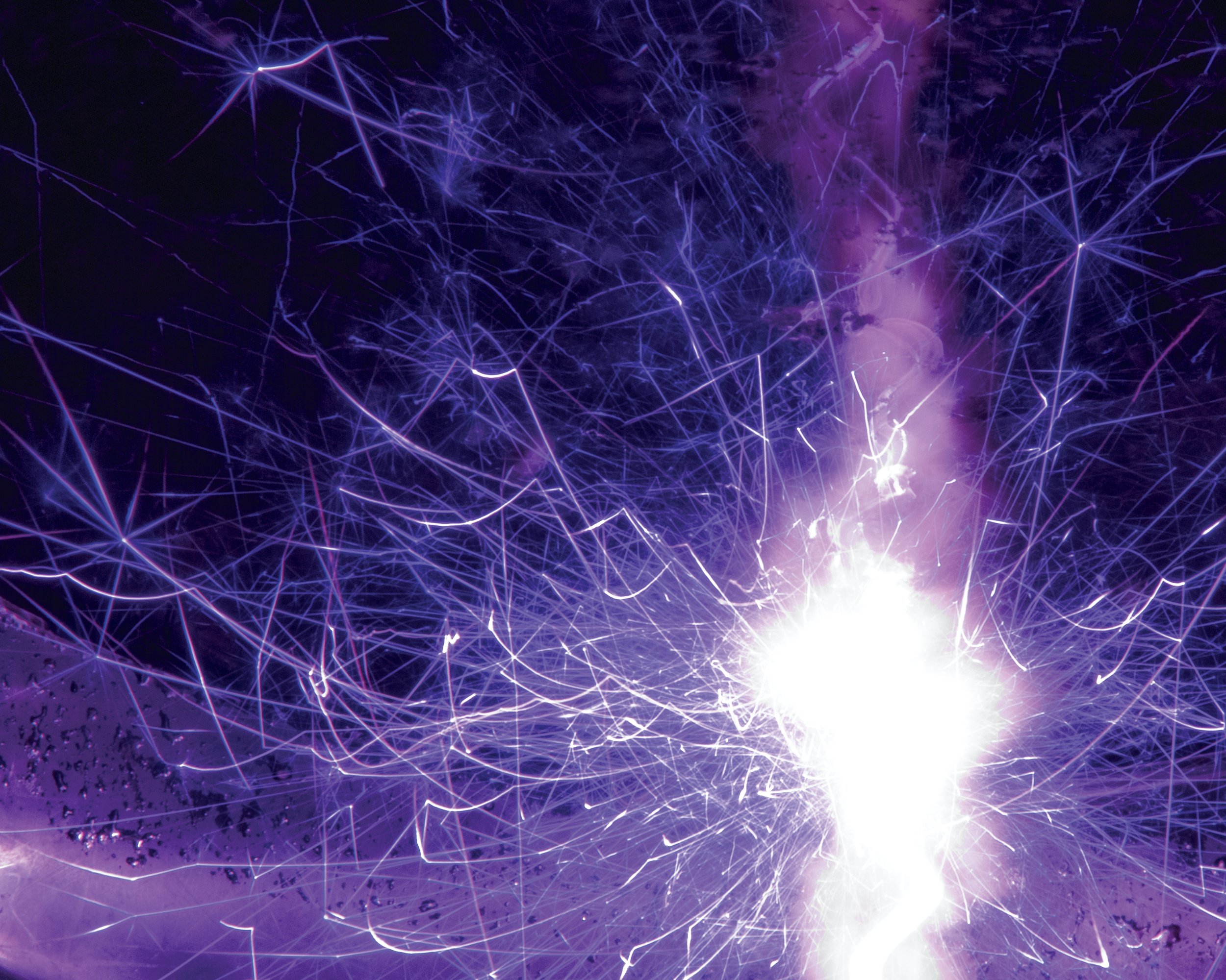 Bright purple and white sparks from a sparkler illuminating a dark background.