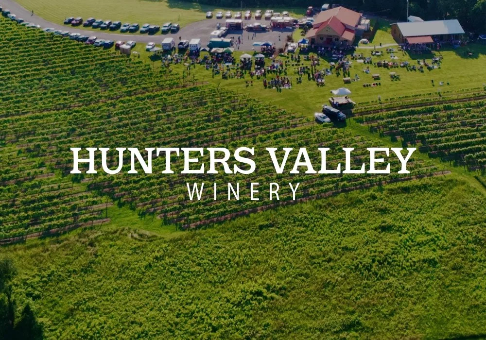 Aerial view of Hunters Valley Winery showing rows of vineyards, the tasting room, and a crowd gathered for an event.