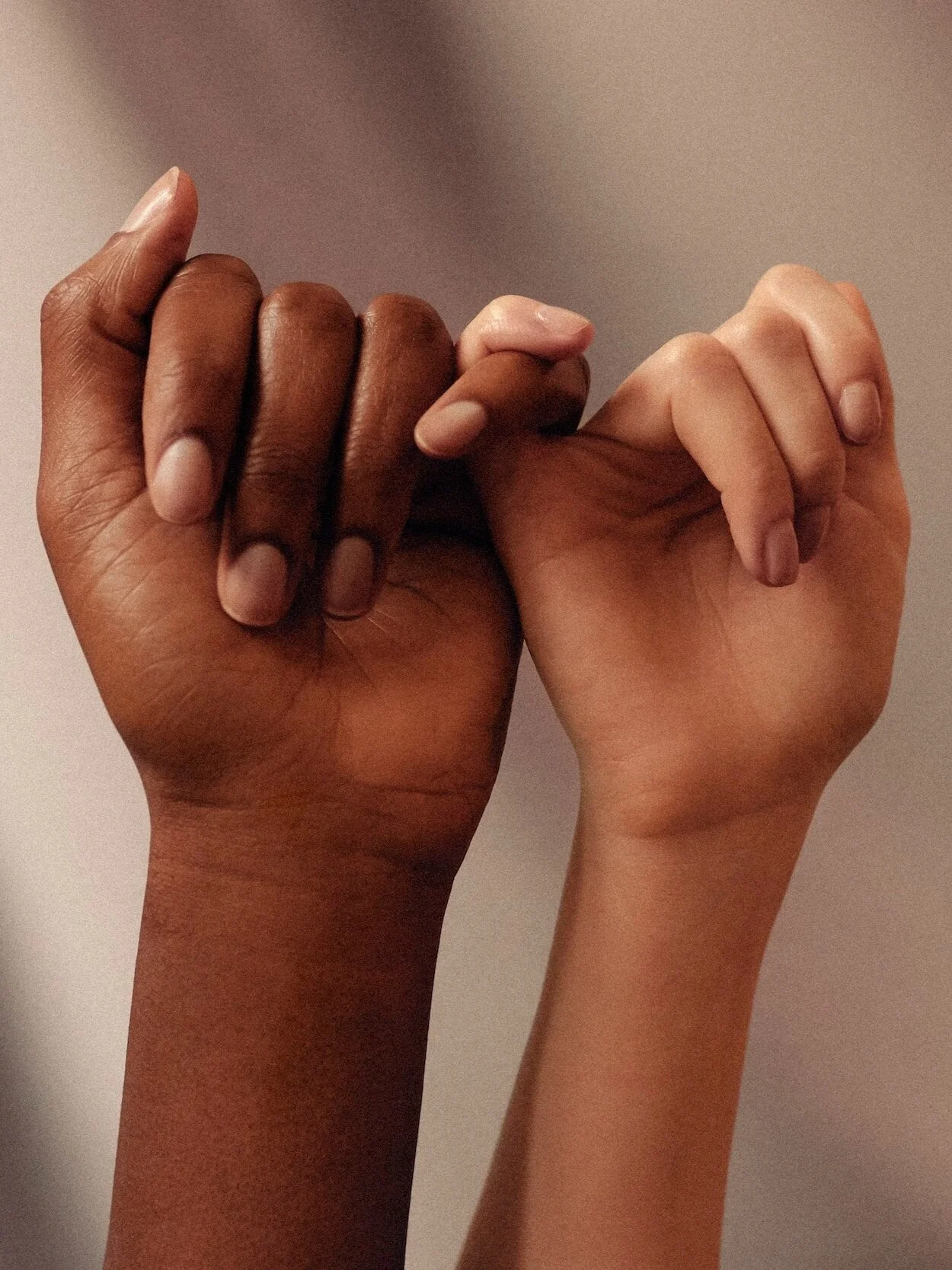 Two hands with different skin tones linking pinky fingers.