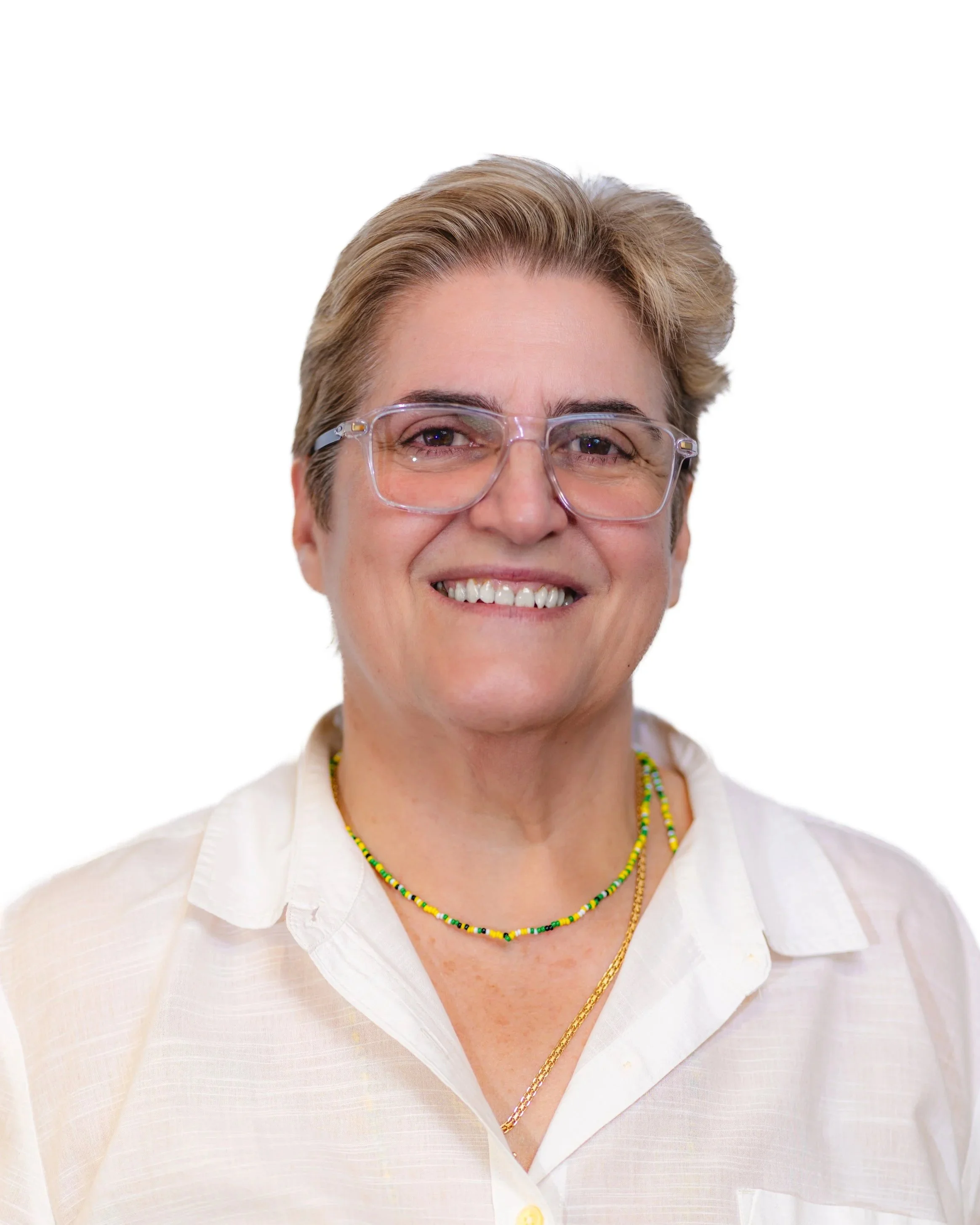 A middle-aged woman with short, brown hair, wearing glasses and a white collared shirt, smiling at the camera against a plain wall background.