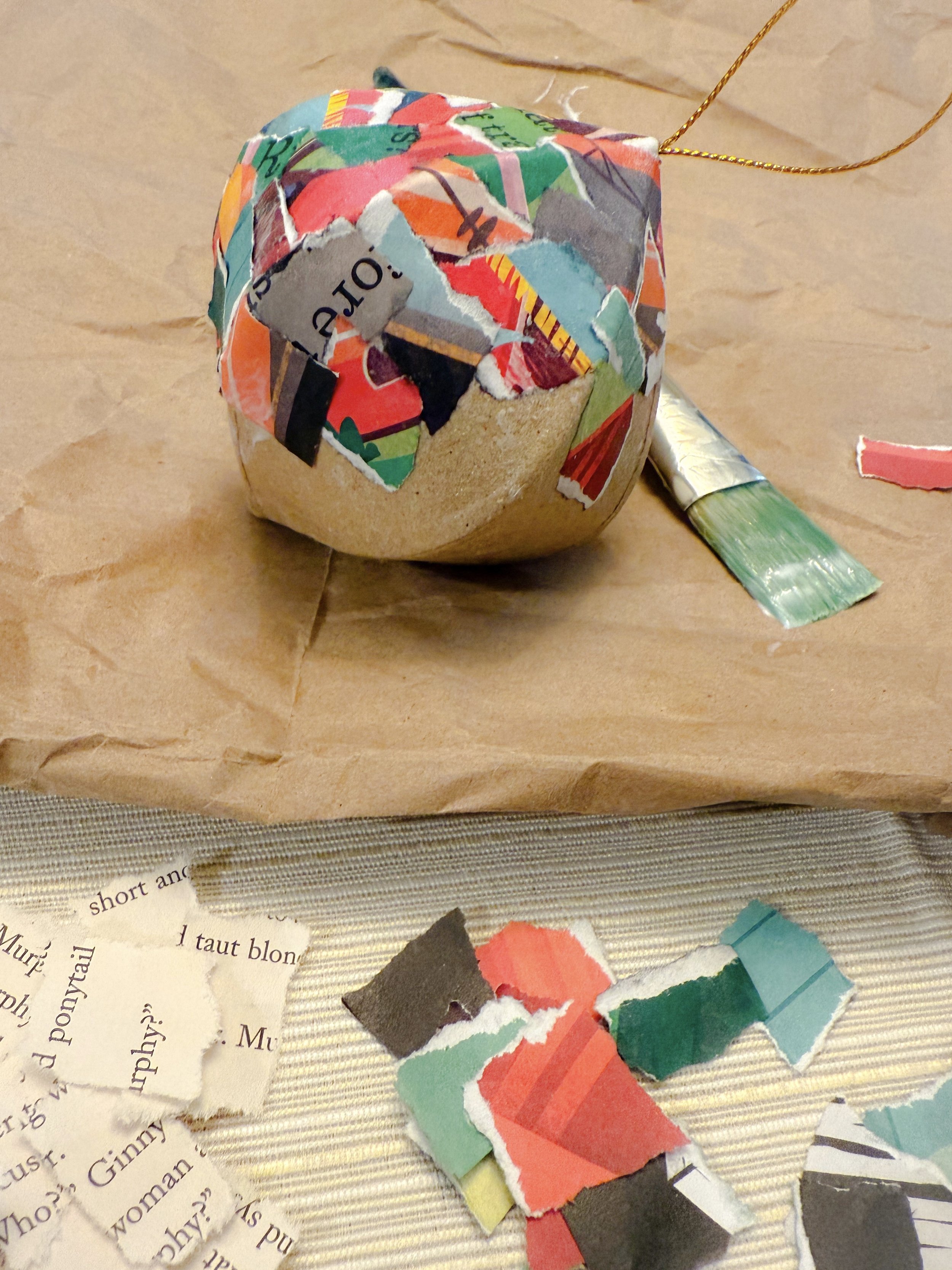 In-progress DIY ornament covered in colorful torn book page pieces, a seasonal family craft project.