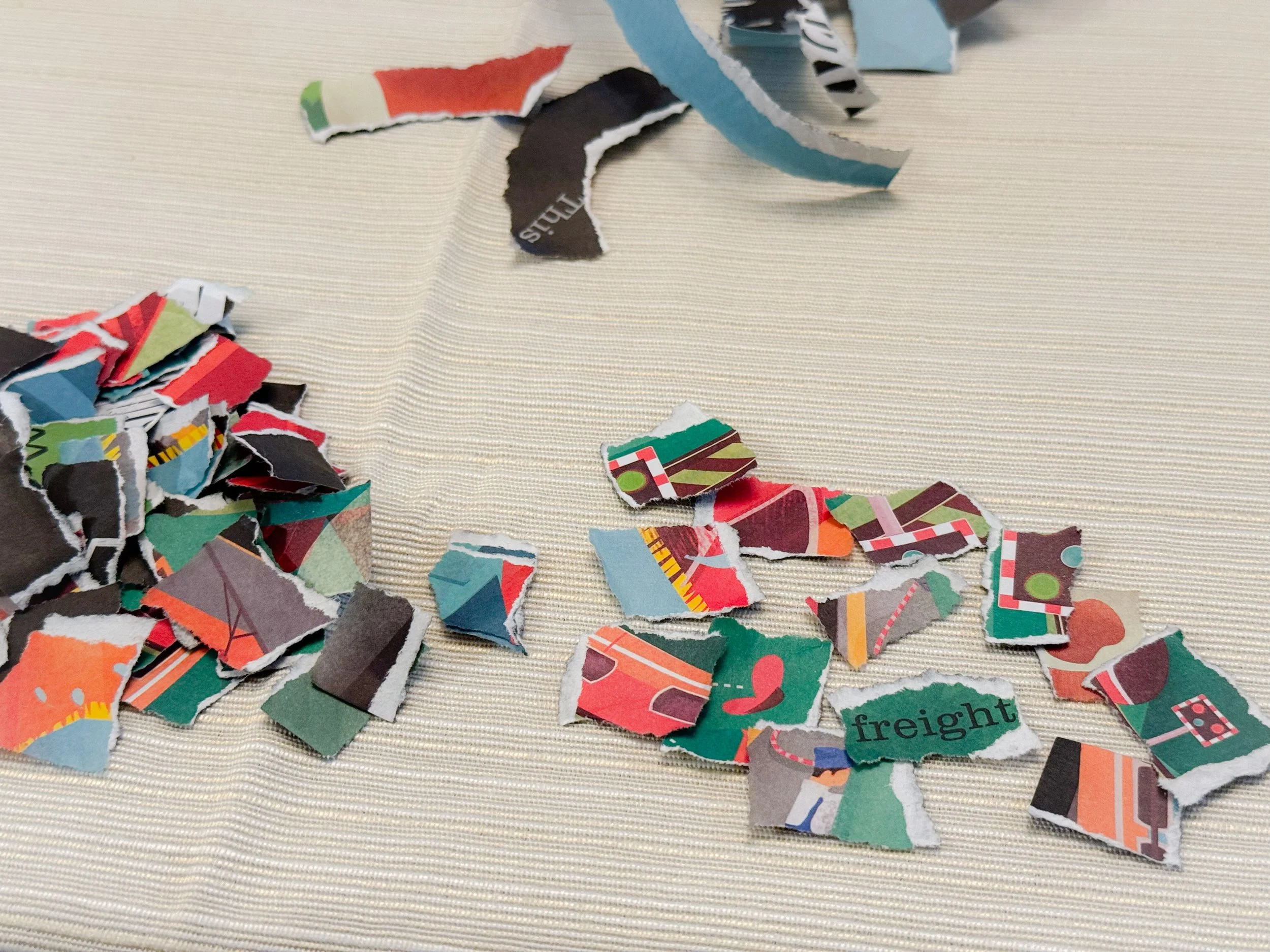 Small torn pieces of colorful picture book pages spread on a table, sorted into piles for making book page ornaments.