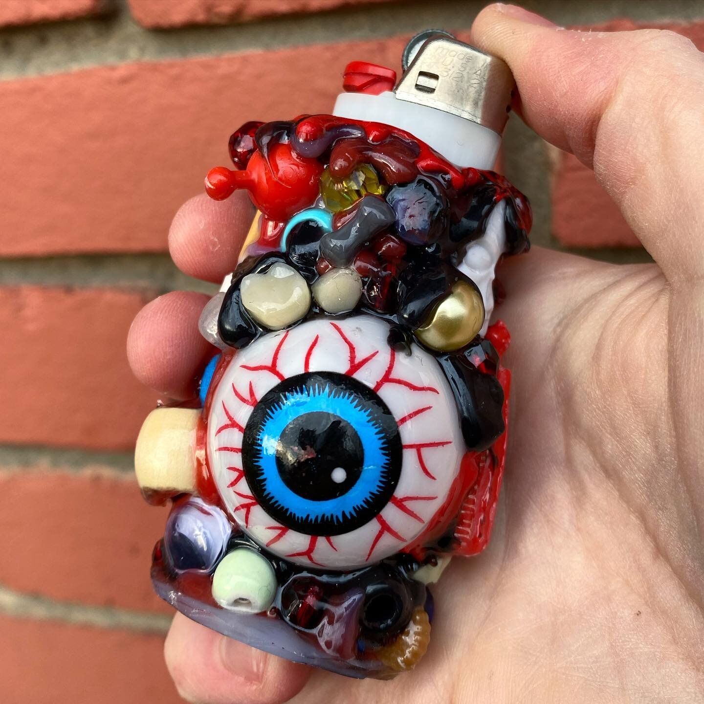 👁️ EYEBOL 🔥 available now, this ooey gooey one of a kind lighter case featuring spooky teefs and skele bones 😮 on sale now for only 25 human earth doll hairs! link in bio to scoop 🔥 iamrisik.com/beadlejuice-products