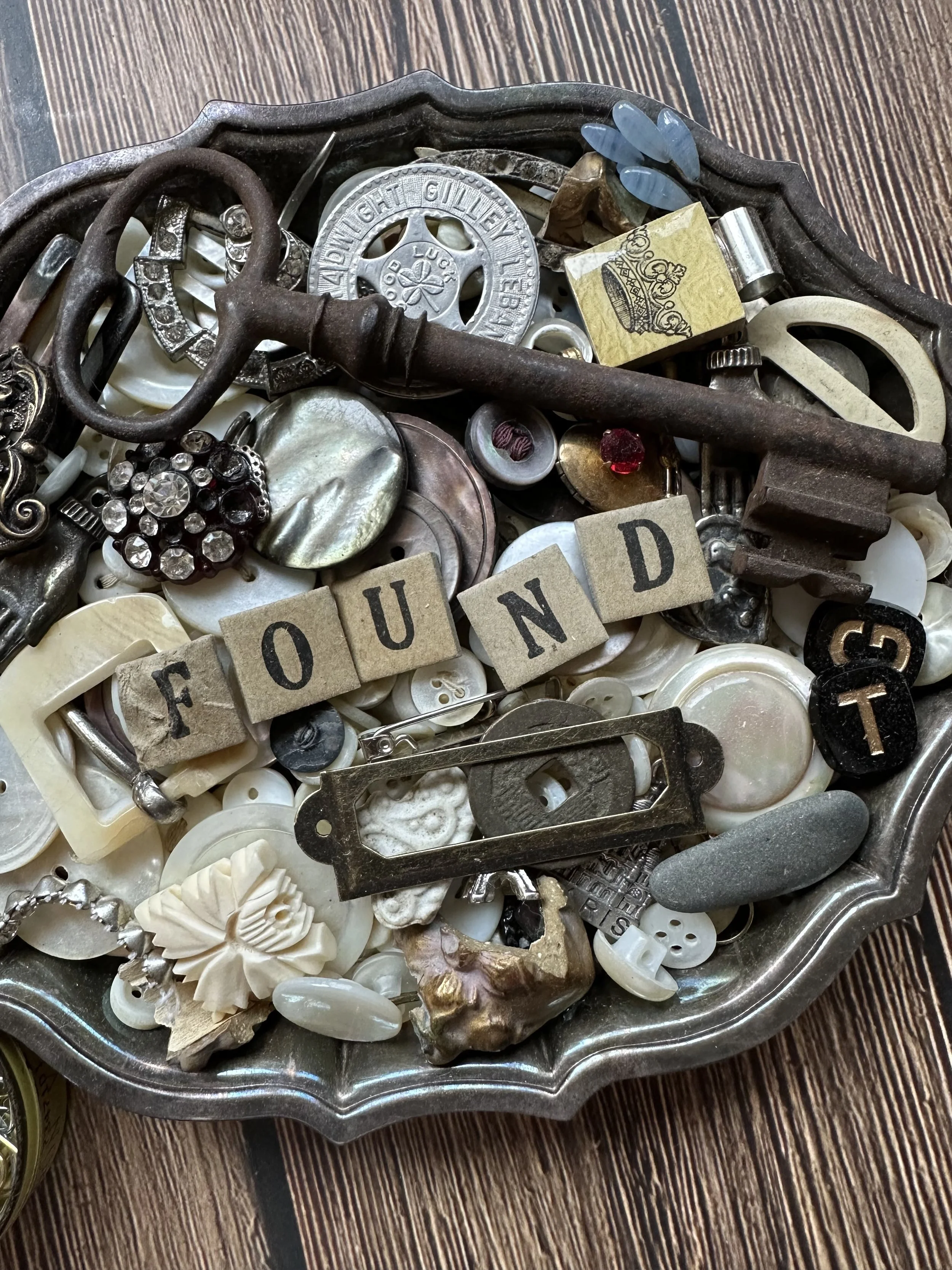 "silver dish full of buttons, coins, rhinestone jewelry bits, and other found objets"