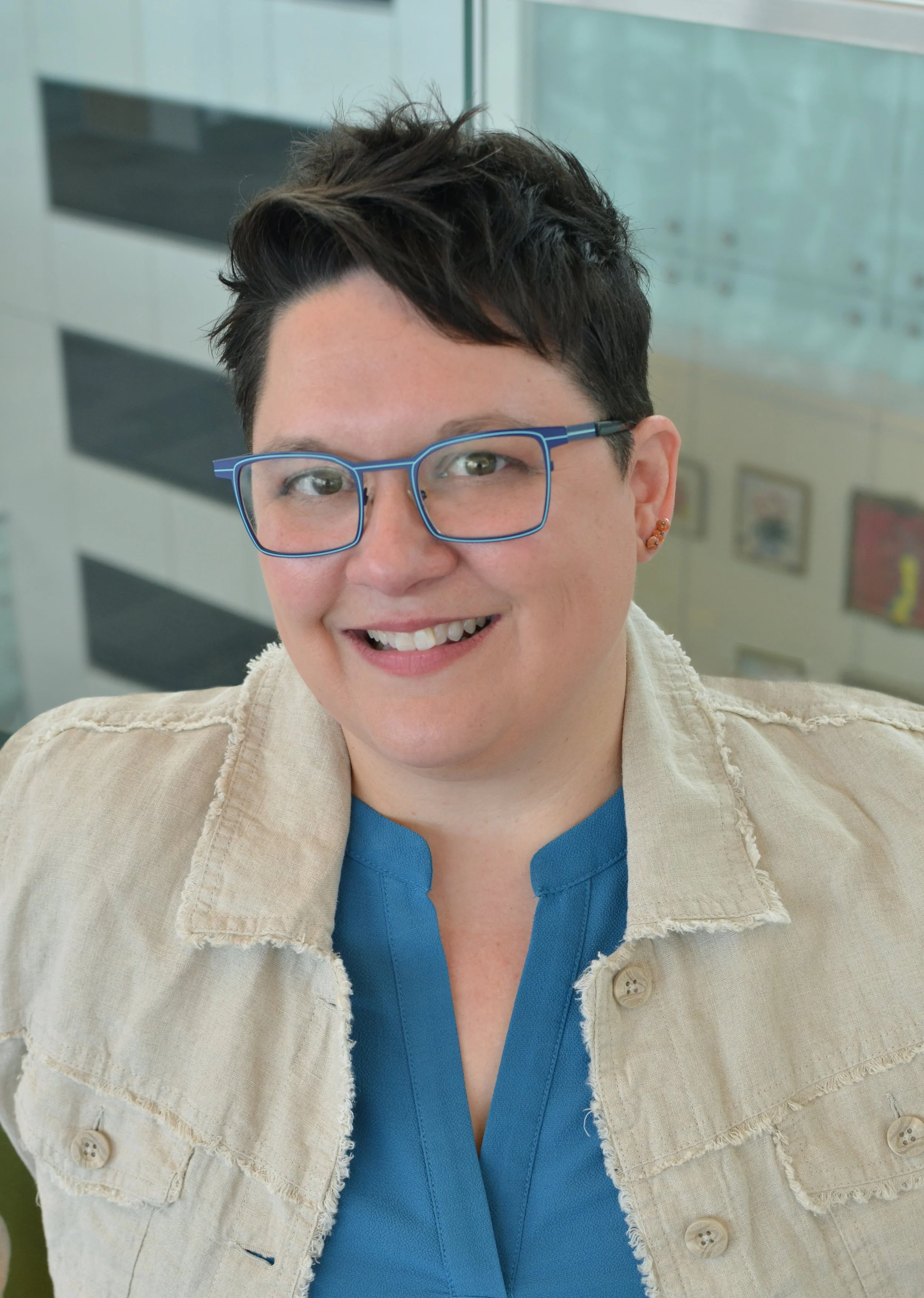 Headshot of Natalie with short dark hair and blue glasses. She is wearing a teal top with a linen jacket.