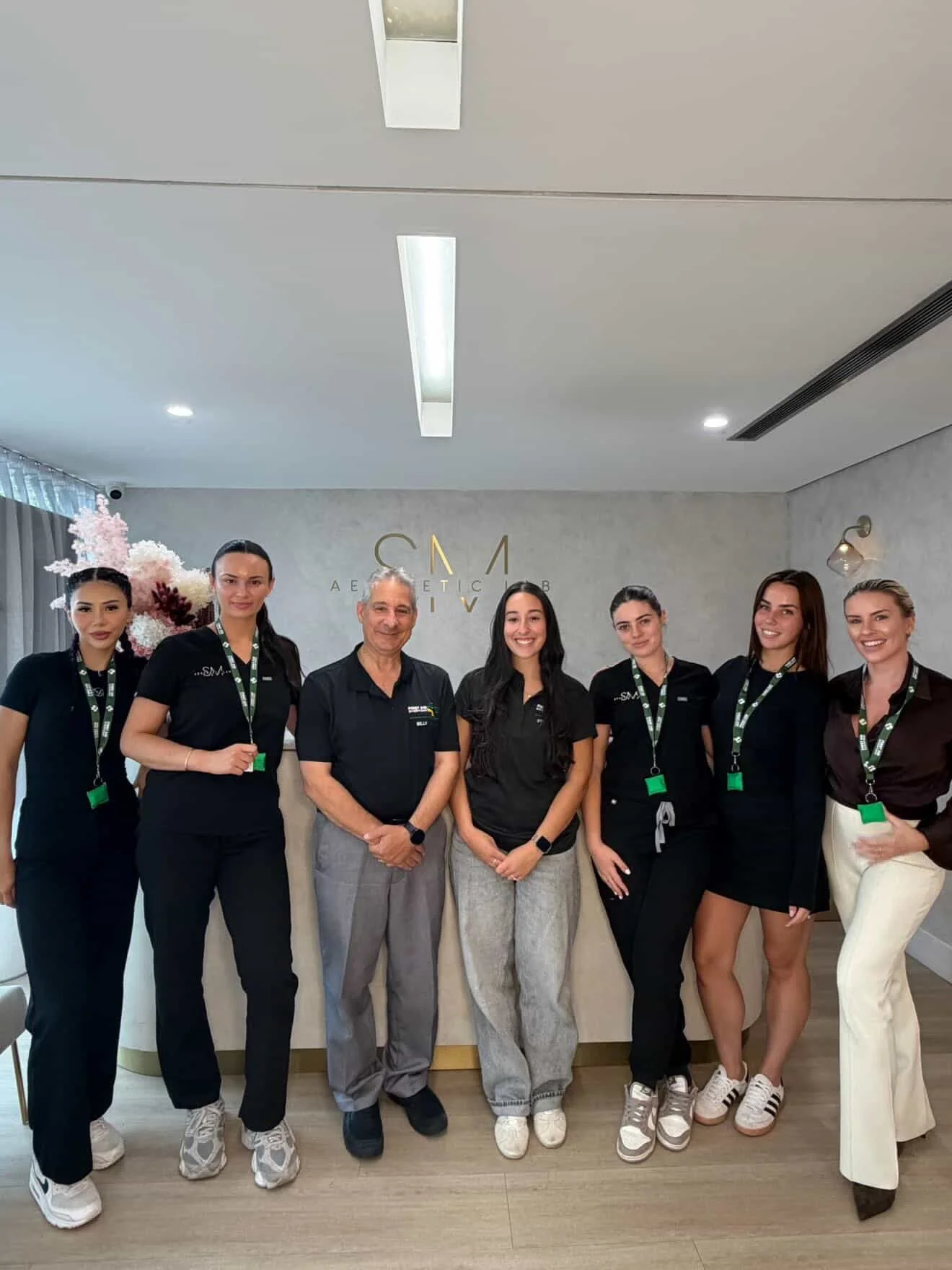 Group of seven staff members, including five women and two men, standing in a clinic or spa reception area, smiling and posing for the photo.