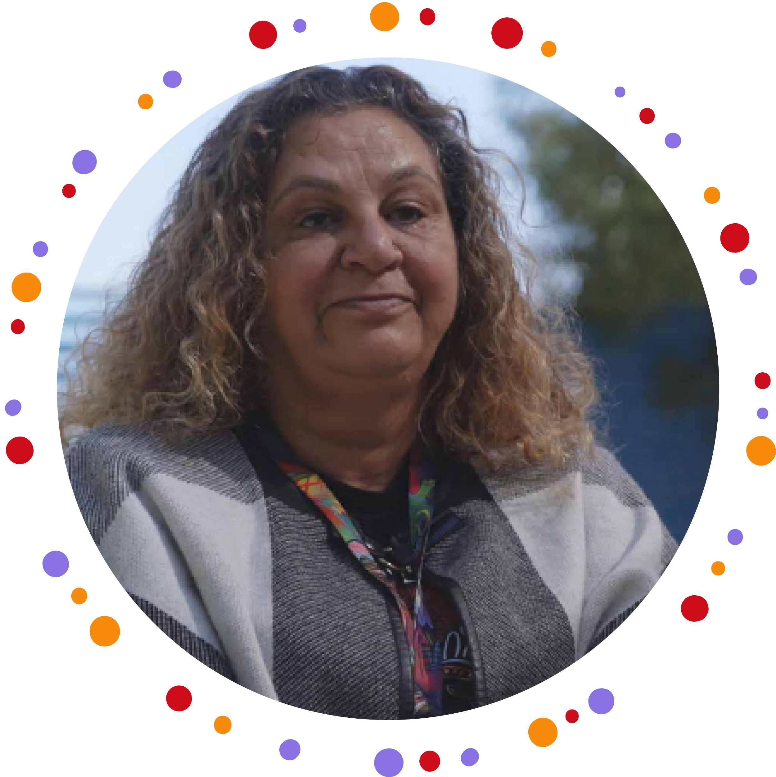 Headshot of Kelli, who has curly brown hair and light brown skin, wearing a jacket and a lanyard and smiling.